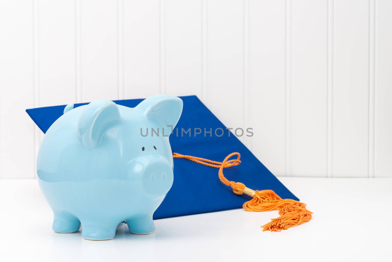 Blue piggy bank and graduation cap.  Conveys the concept of the cost of higher education.
