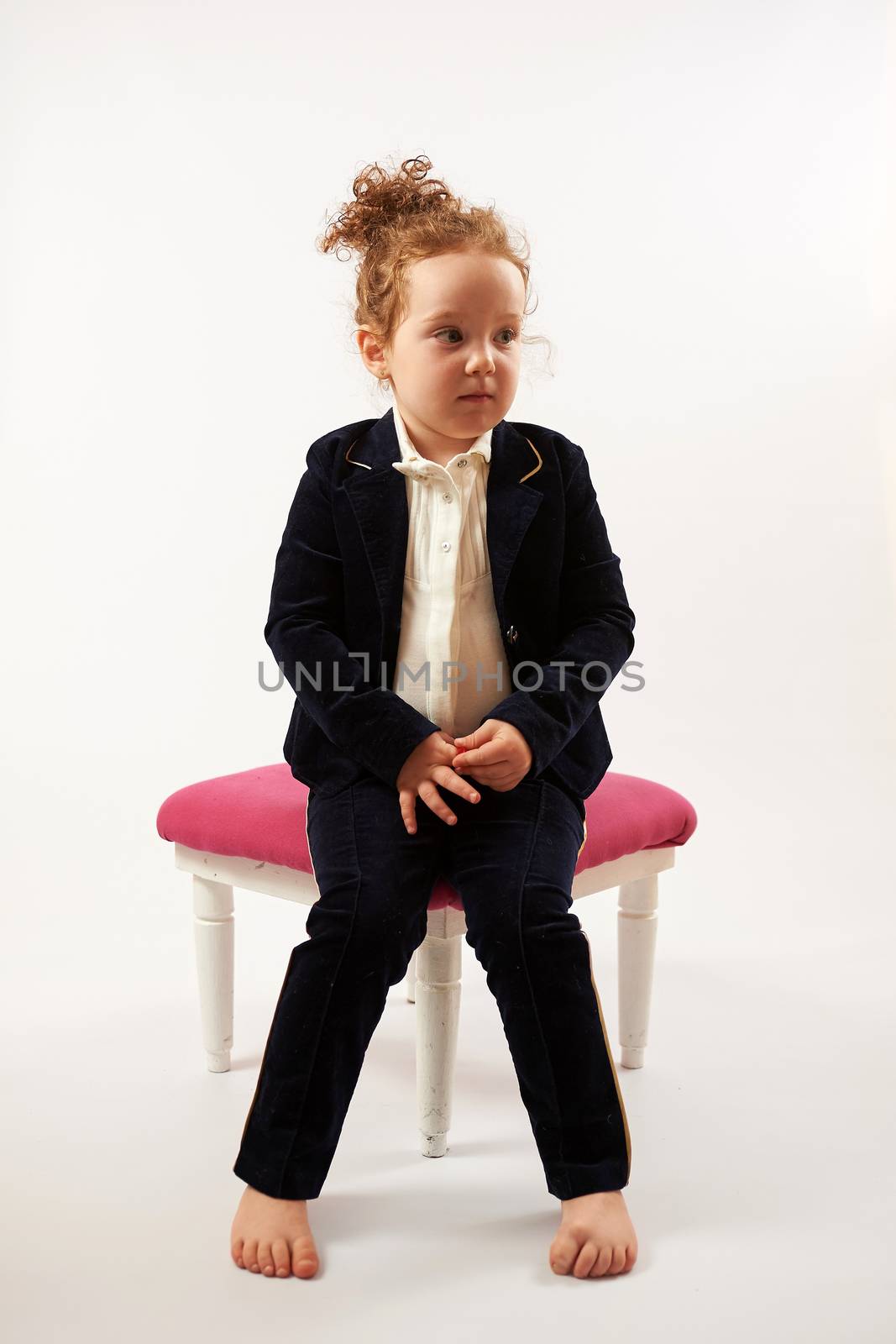 Little girl in black suit sitting on a rose stool