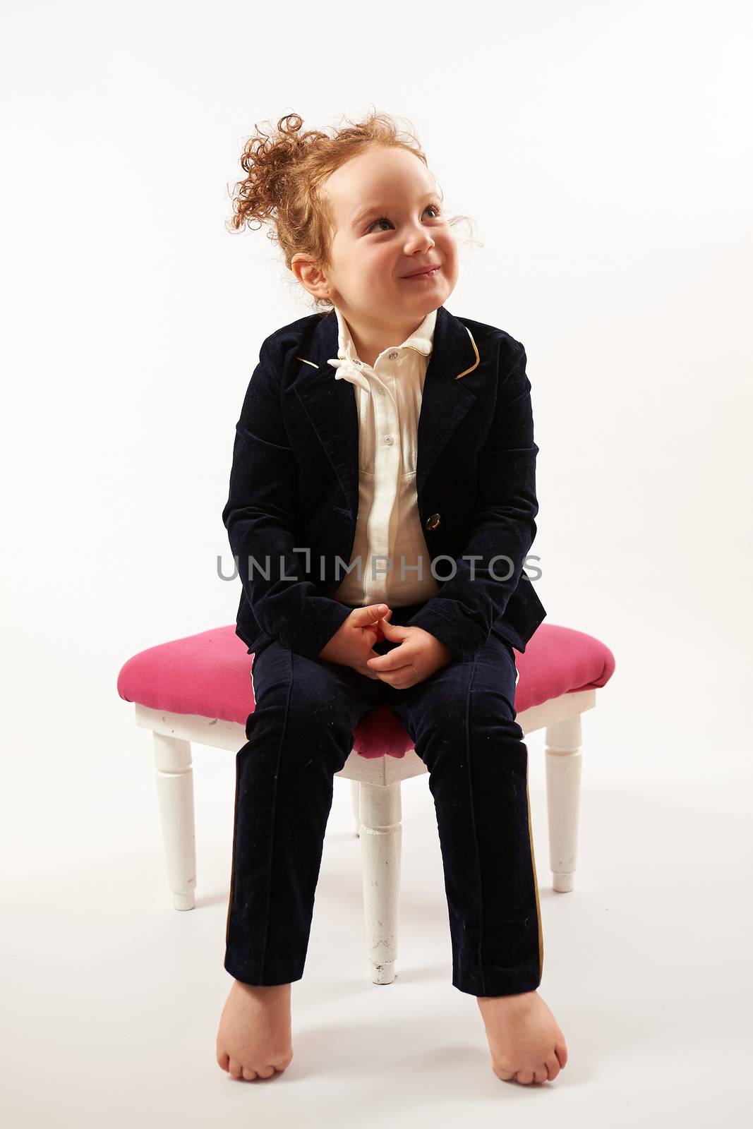 Little girl in black suit sitting on a rose stool and pouting