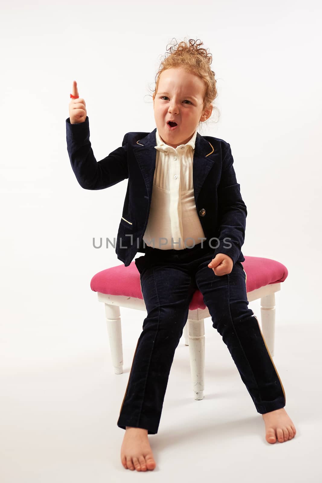 Little girl in black suit sitting and shows up.