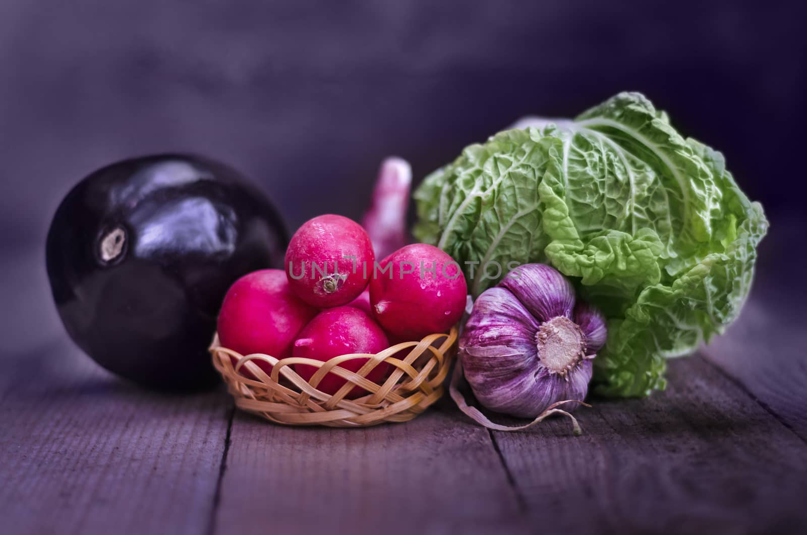 Radishes,garlic,cabbage and eggplant, on the old boards and blurred background. Rustic style, stained in purple color.
