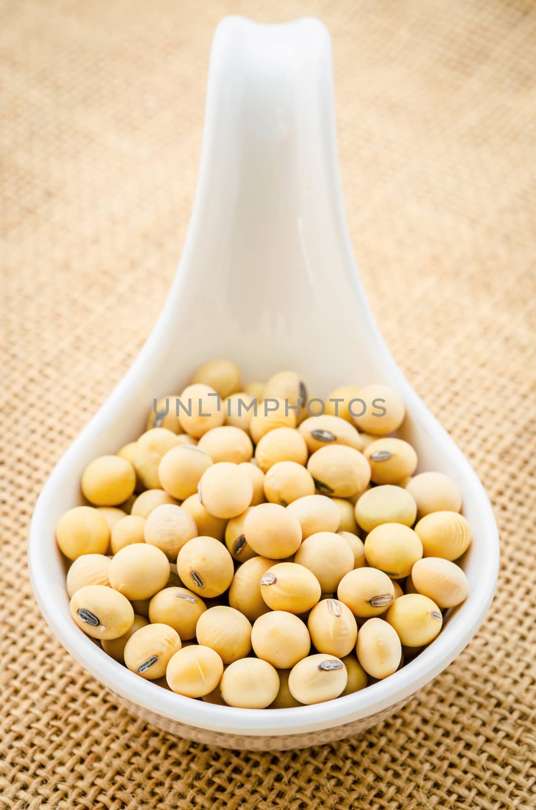 Soy beans in white spoon on sack background.