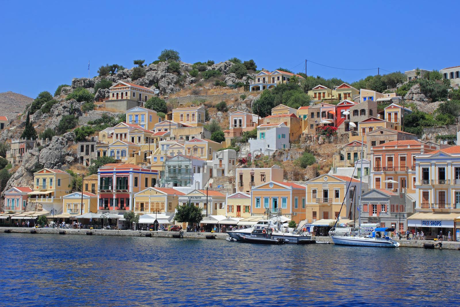 Colorful greek style houses on mountain wall by the sea. Blue sky in background.