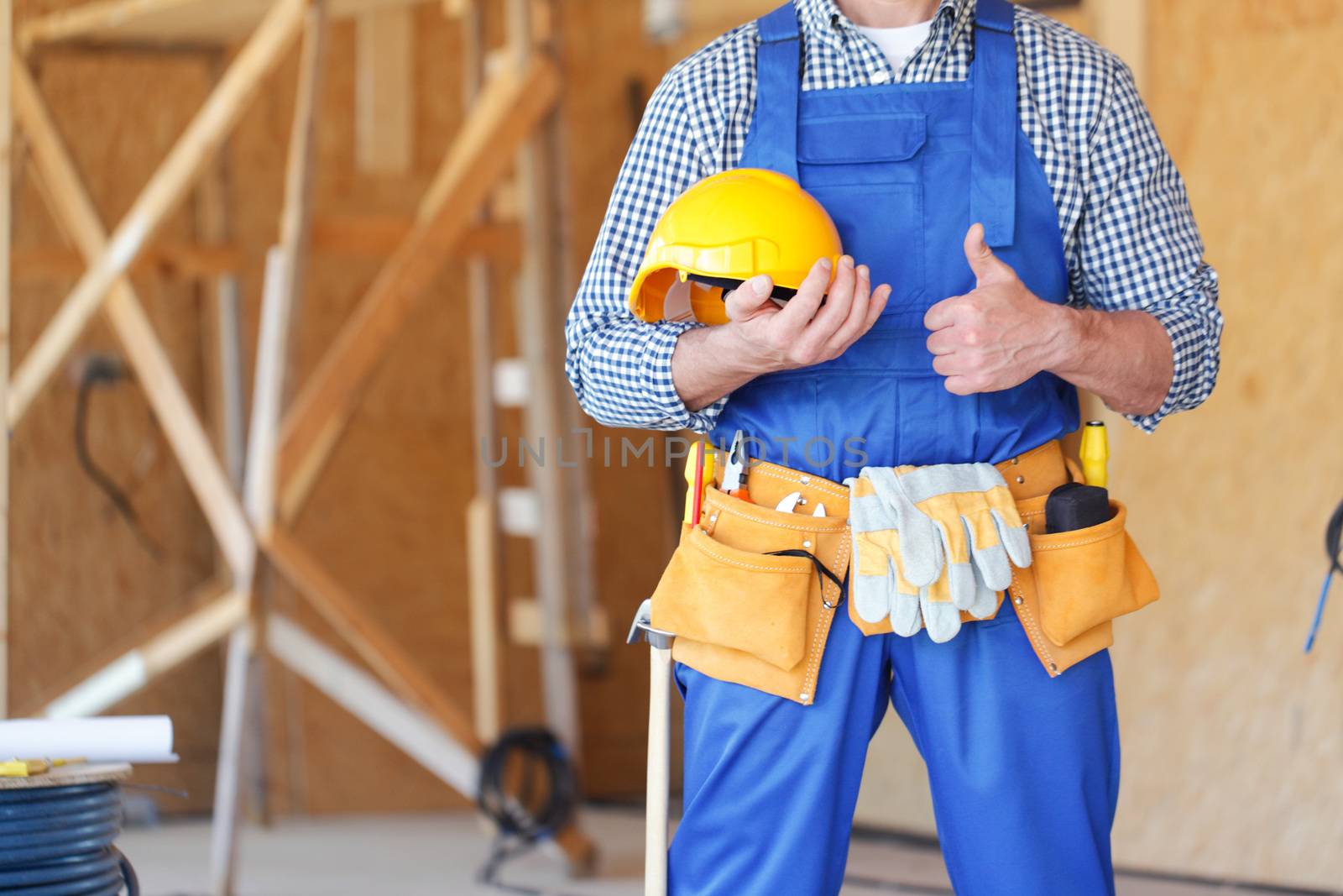 Builder holding hardhat with thumb up at construstion site