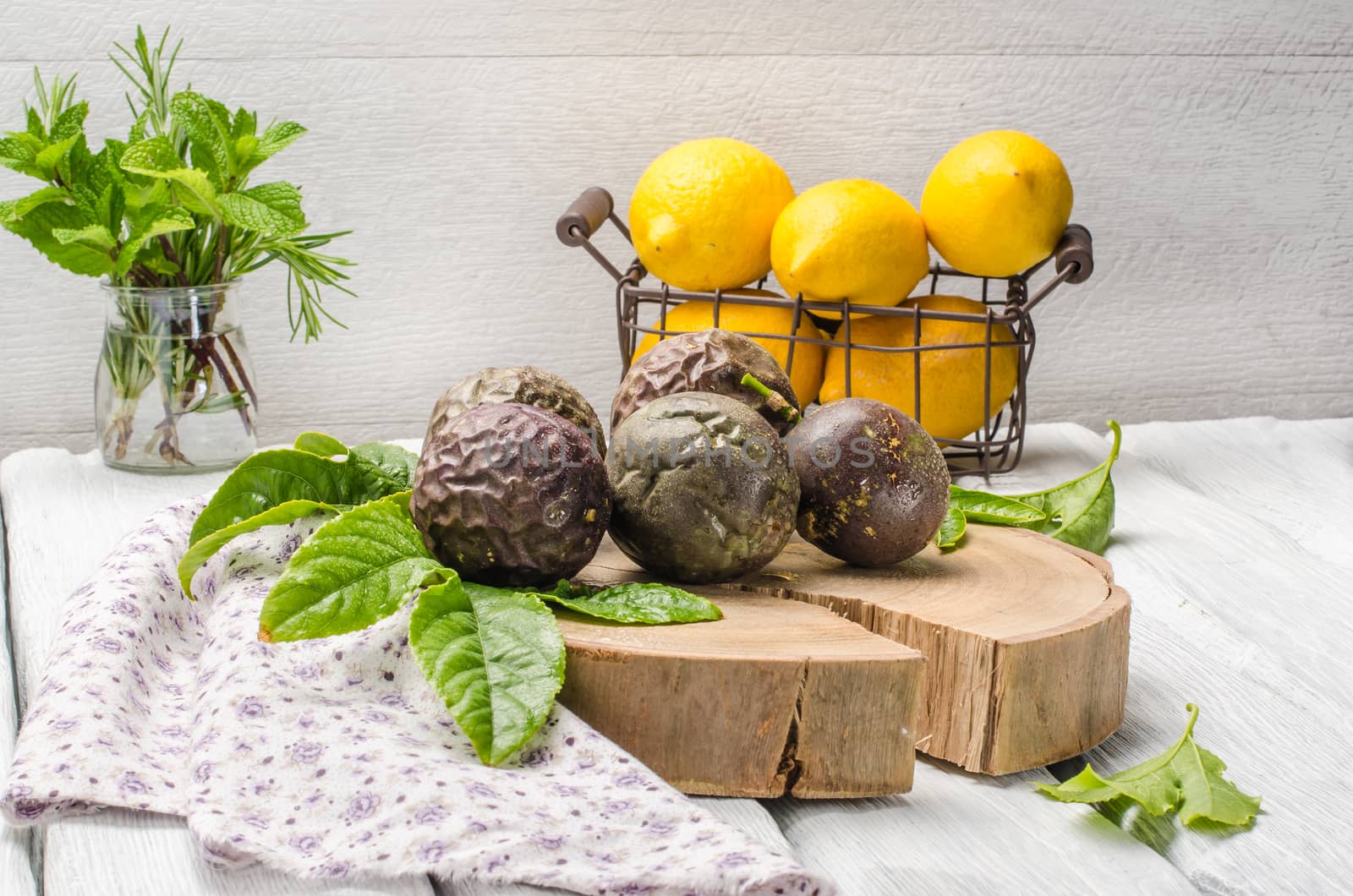 Passion fruits with leaves, lemons and herbs in jar on the vintage wooden table.
