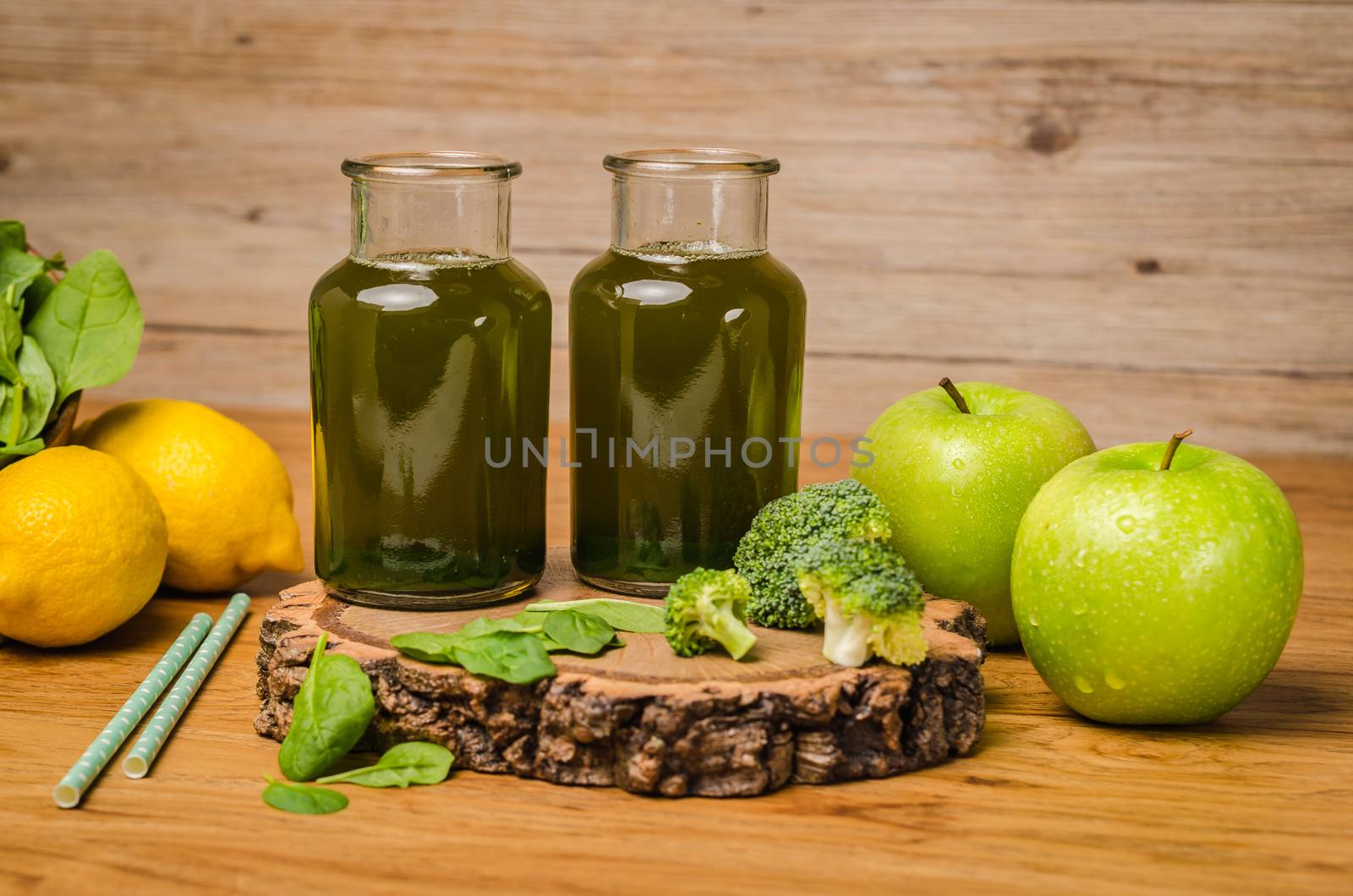 Green fresh leafy greens smoothie in glass jar, spinach leaves, apple, broccoli and lemon. Refreshing healthy drink on wooden table background