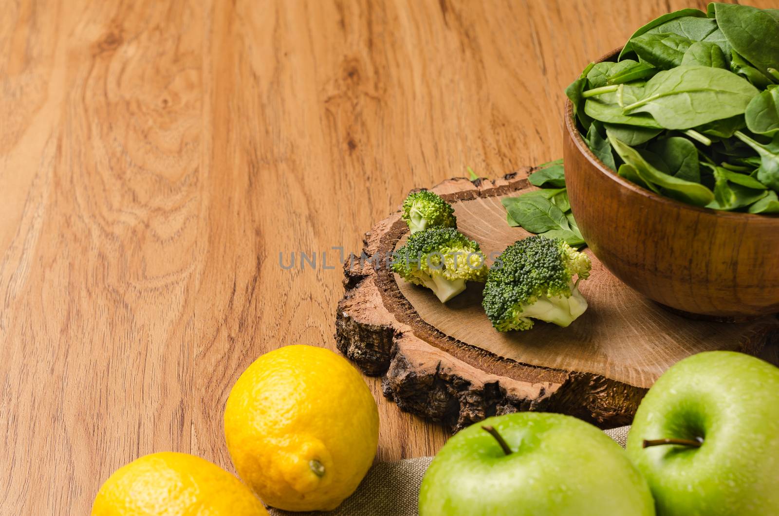 Spring spinach leaves in the bowl, broccoli, lemons and apples on wooden table background