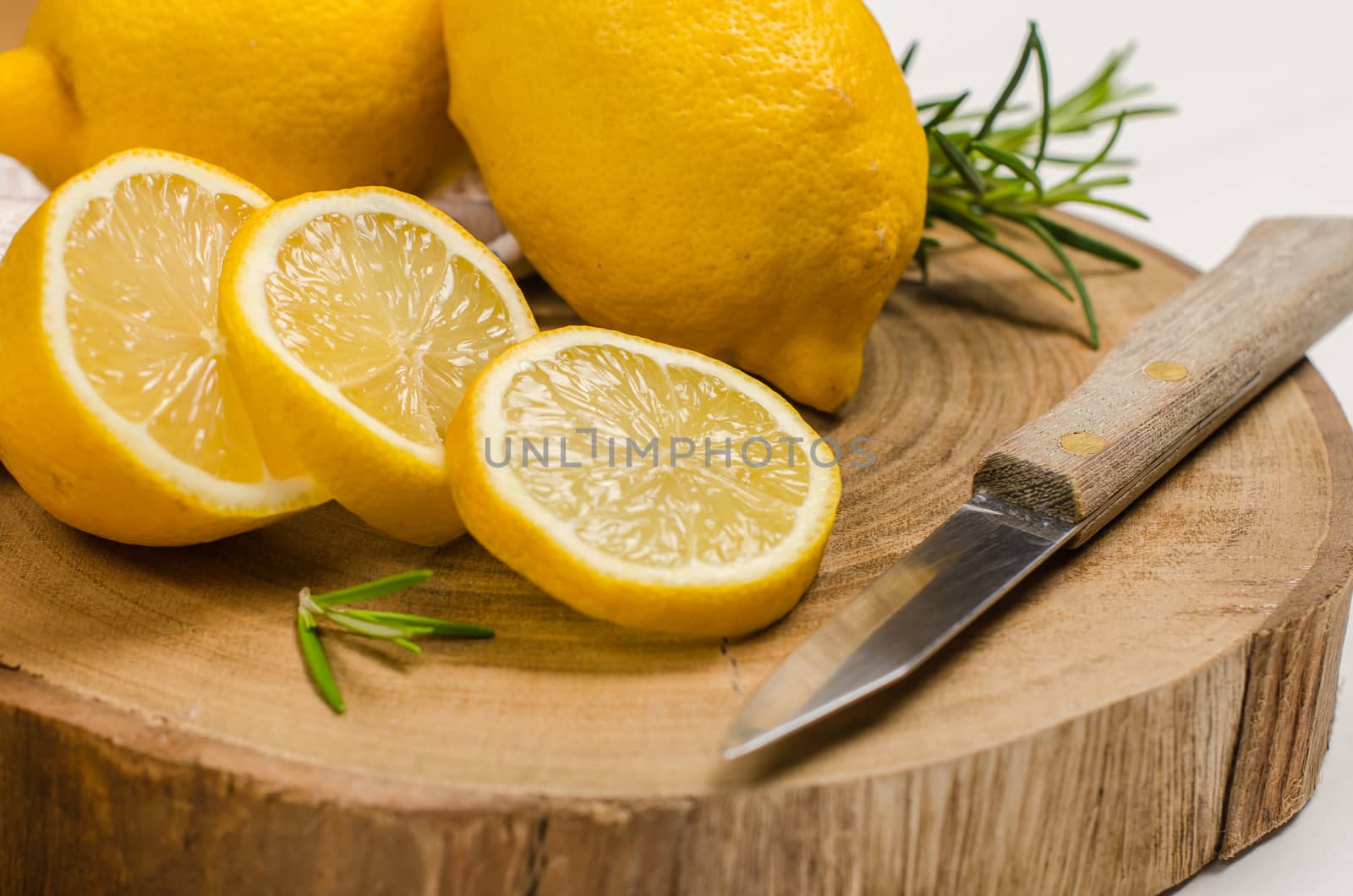 Slices, half fresh juicy lemon with rosemary and knife on the vintage wooden table.