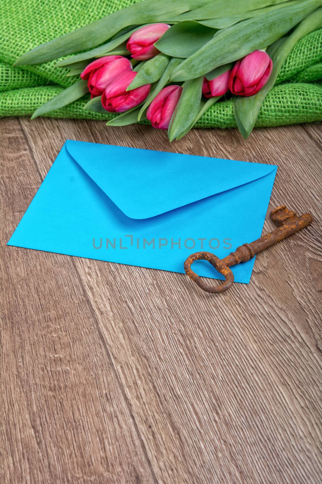 Envelope, rusty key and red tulip on a wooden background