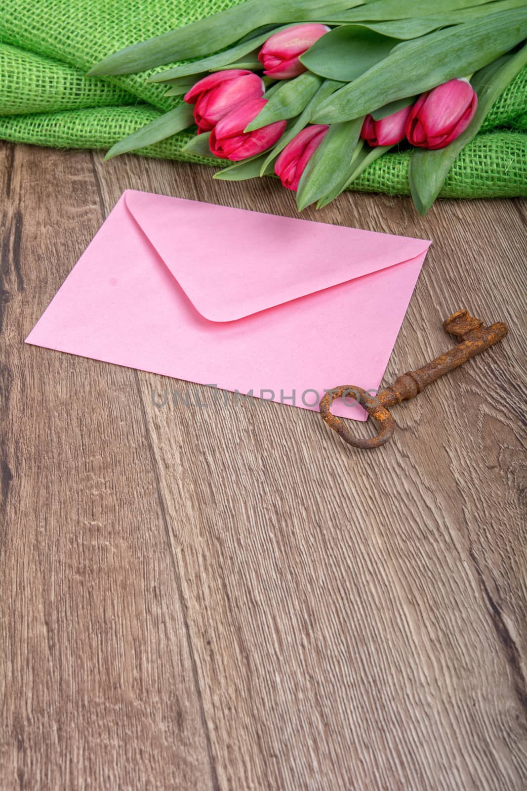 Envelope, rusty key and red tulip on a wooden background