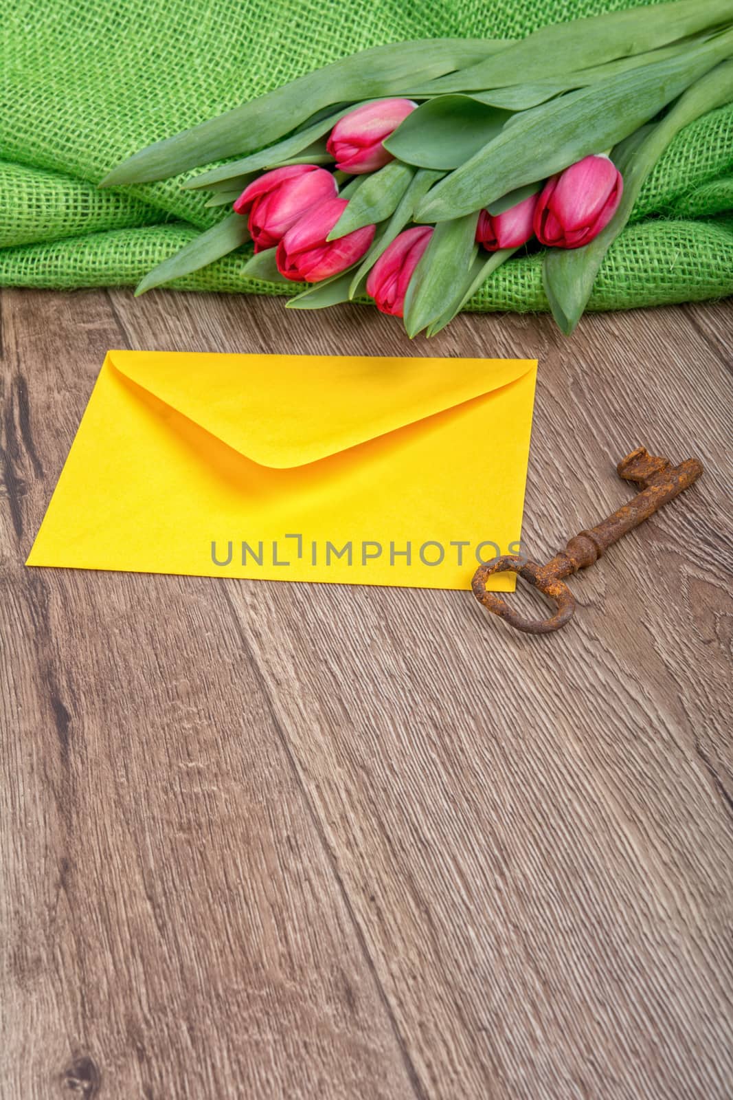 Envelope, rusty key and red tulip on a wooden background