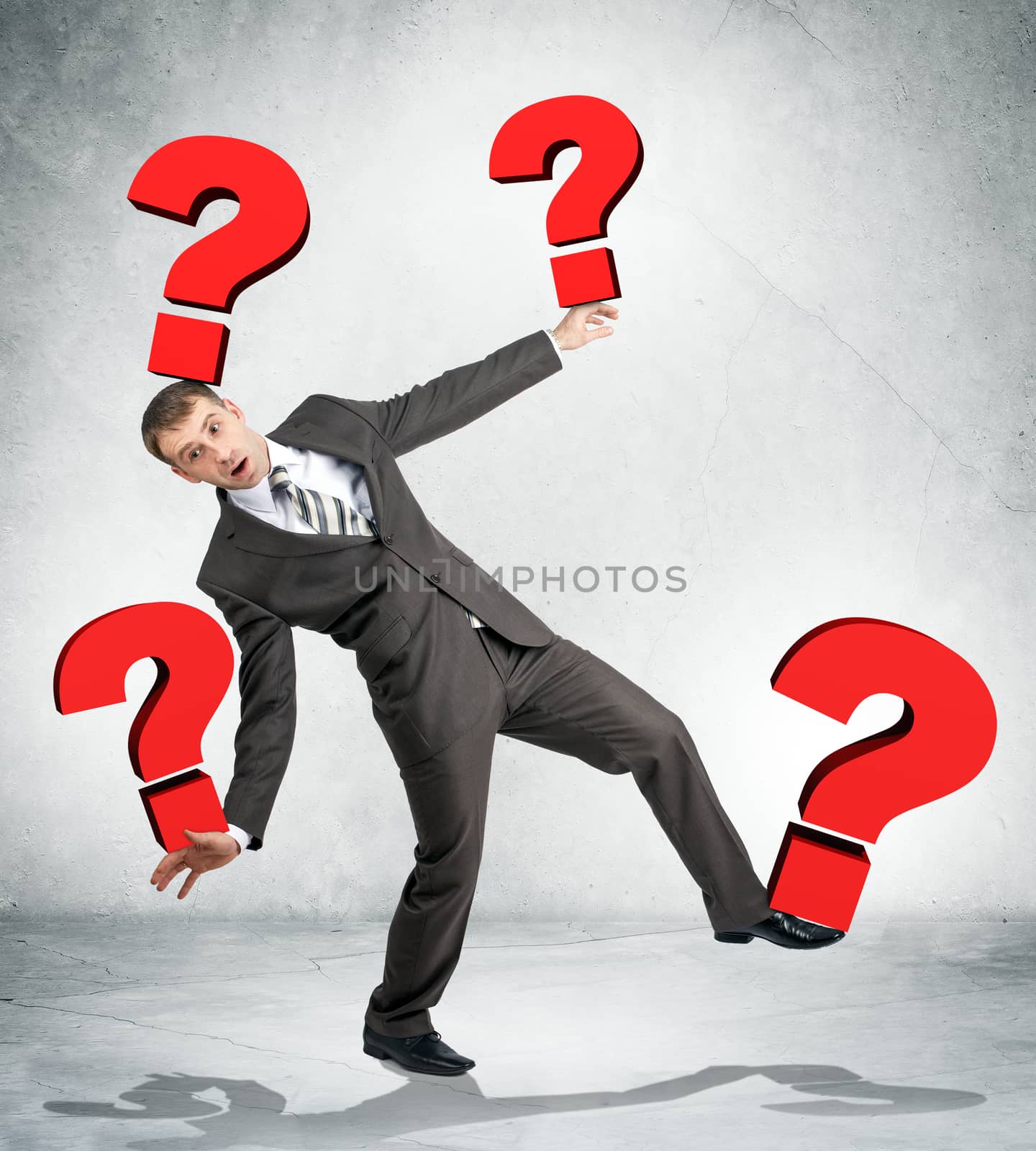 Portrait of businessman holding red question marks on grey wall background