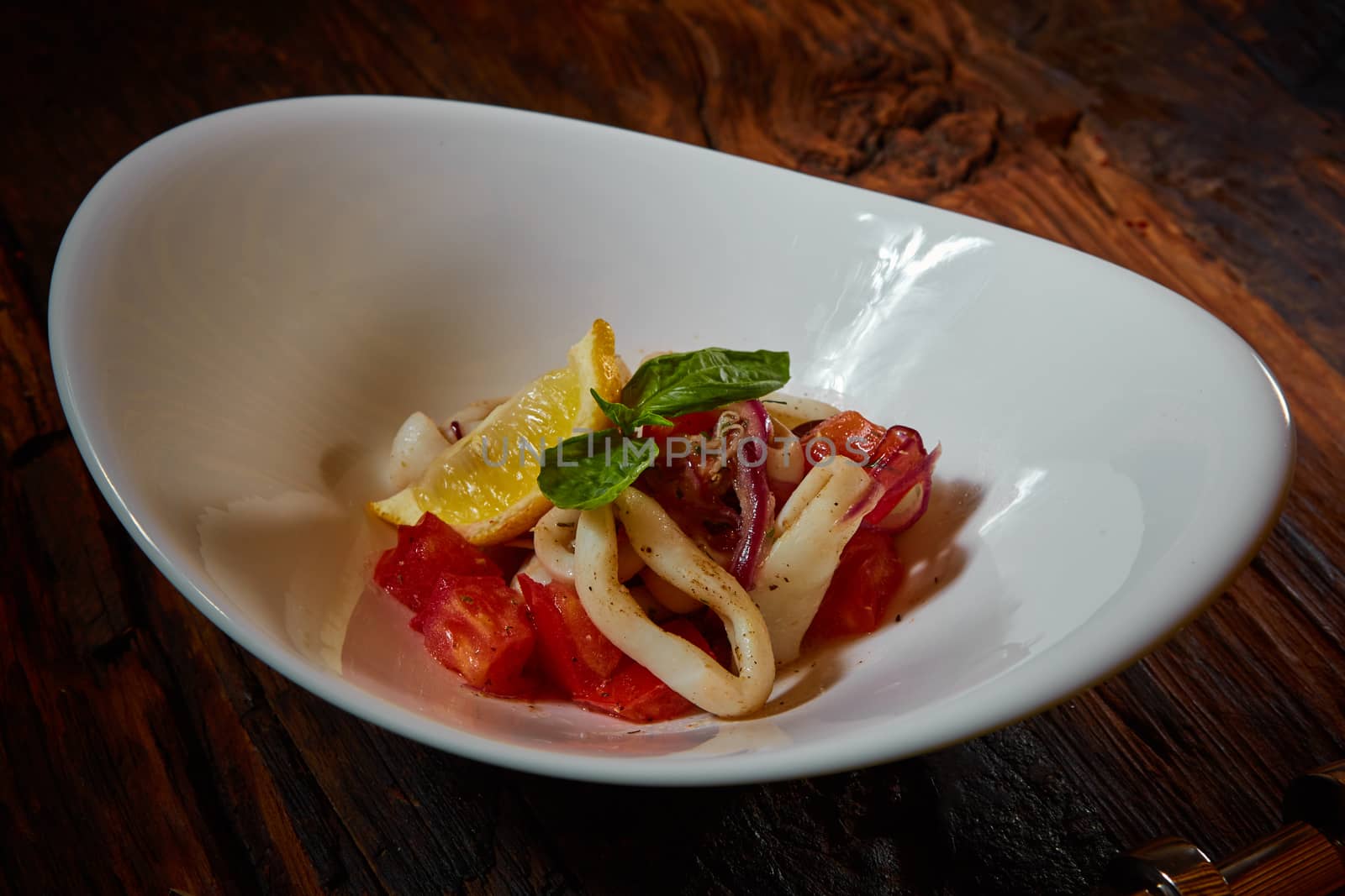 healthy rings squid salad with tomatoes decorated with basil leaves