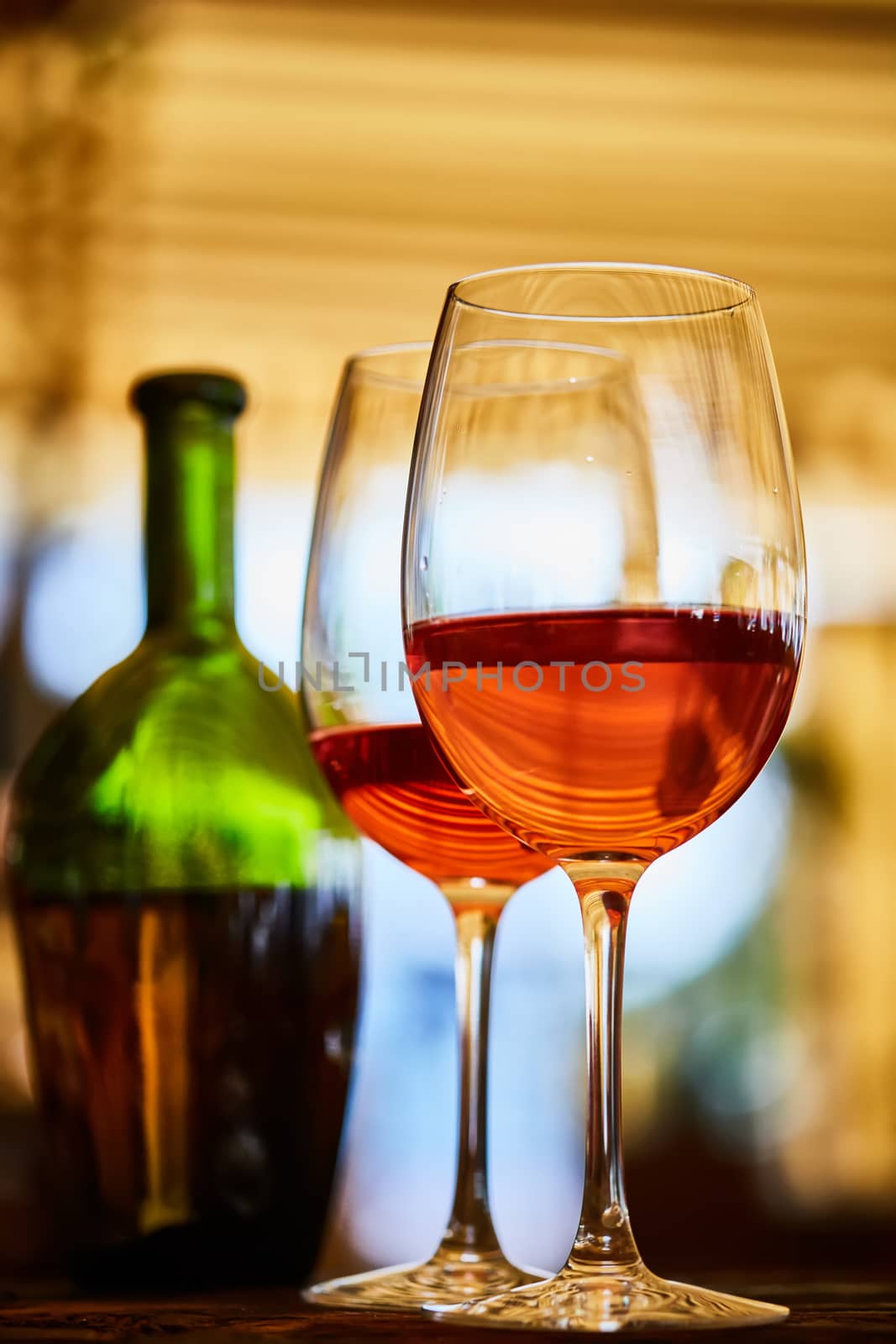 two wine glasses filled with red wine and wine bottle in background. Soft focus