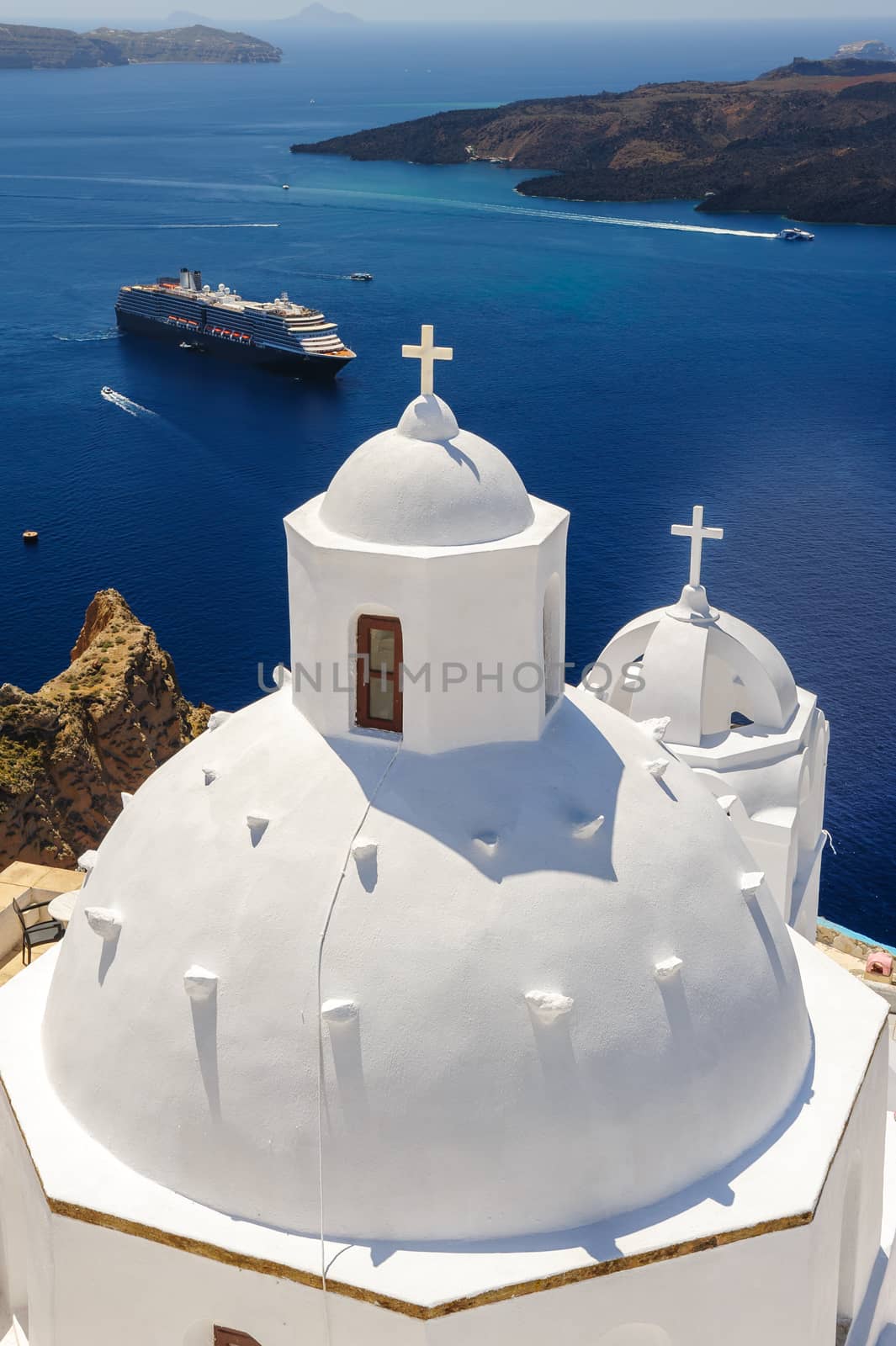 White orthodox church bell tower and sea with ships at background. Fira, Santorini Greece. Copyspace