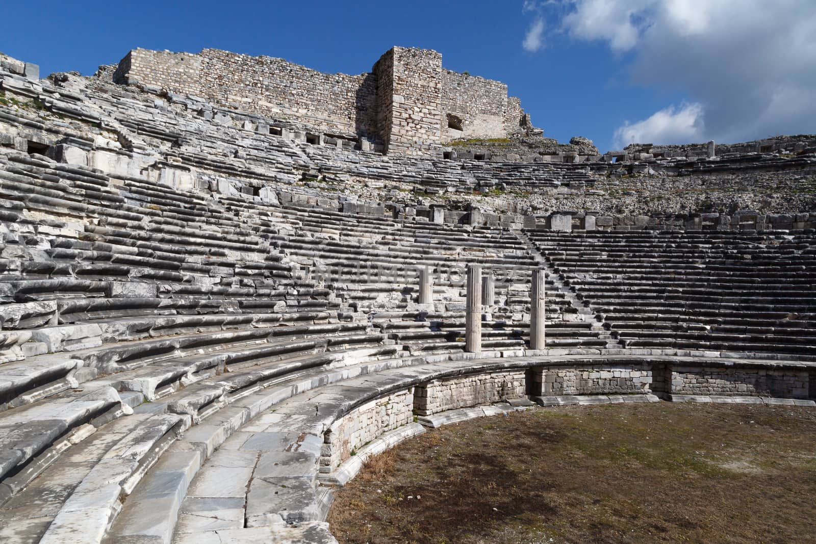 View of Miletus amphitheater in Aydin, Turkey with stone stairs on bright blue sky background.