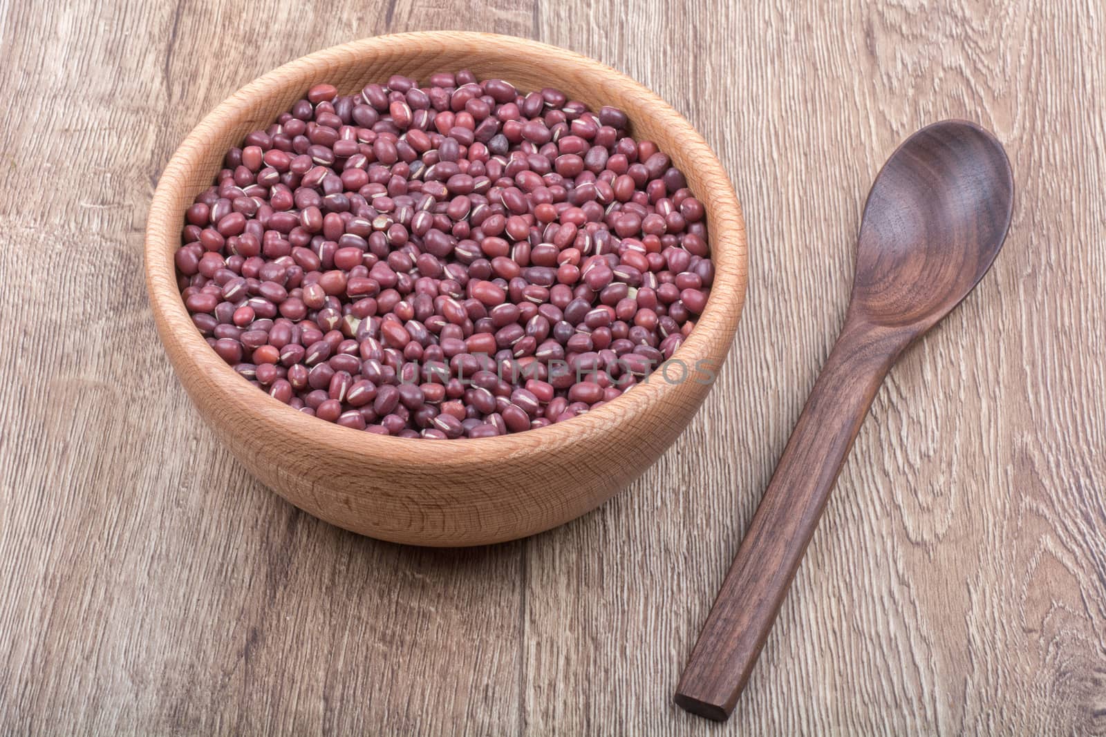 Bowl with beans and wooden spoon on a brown wooden background