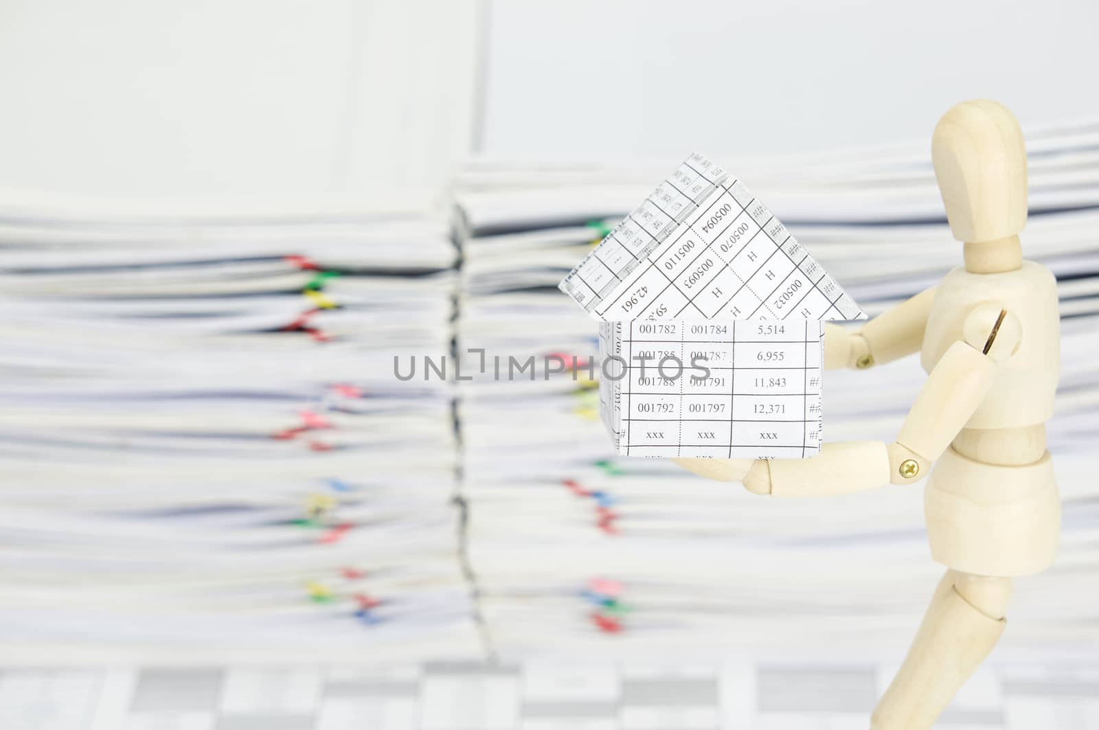 Wooden dummy holding house on finance account have blur overload of paperwork as background.