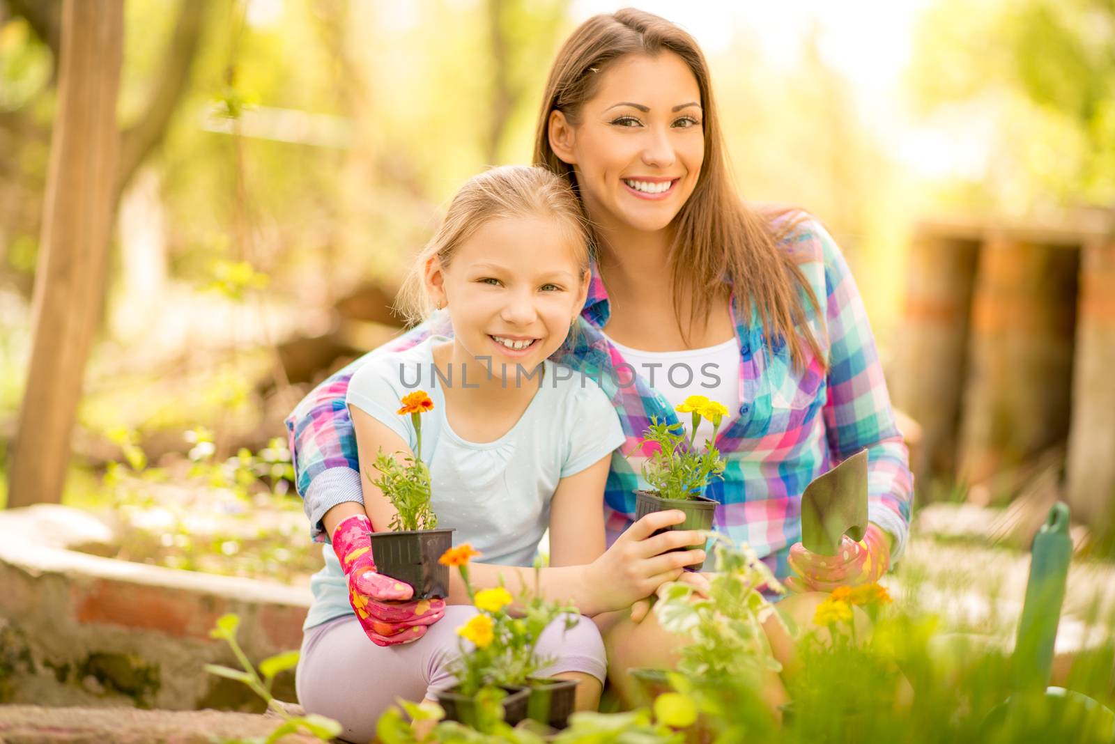 Cute little girl assisting her mother planting flowers in a backyard. Looking at camera.