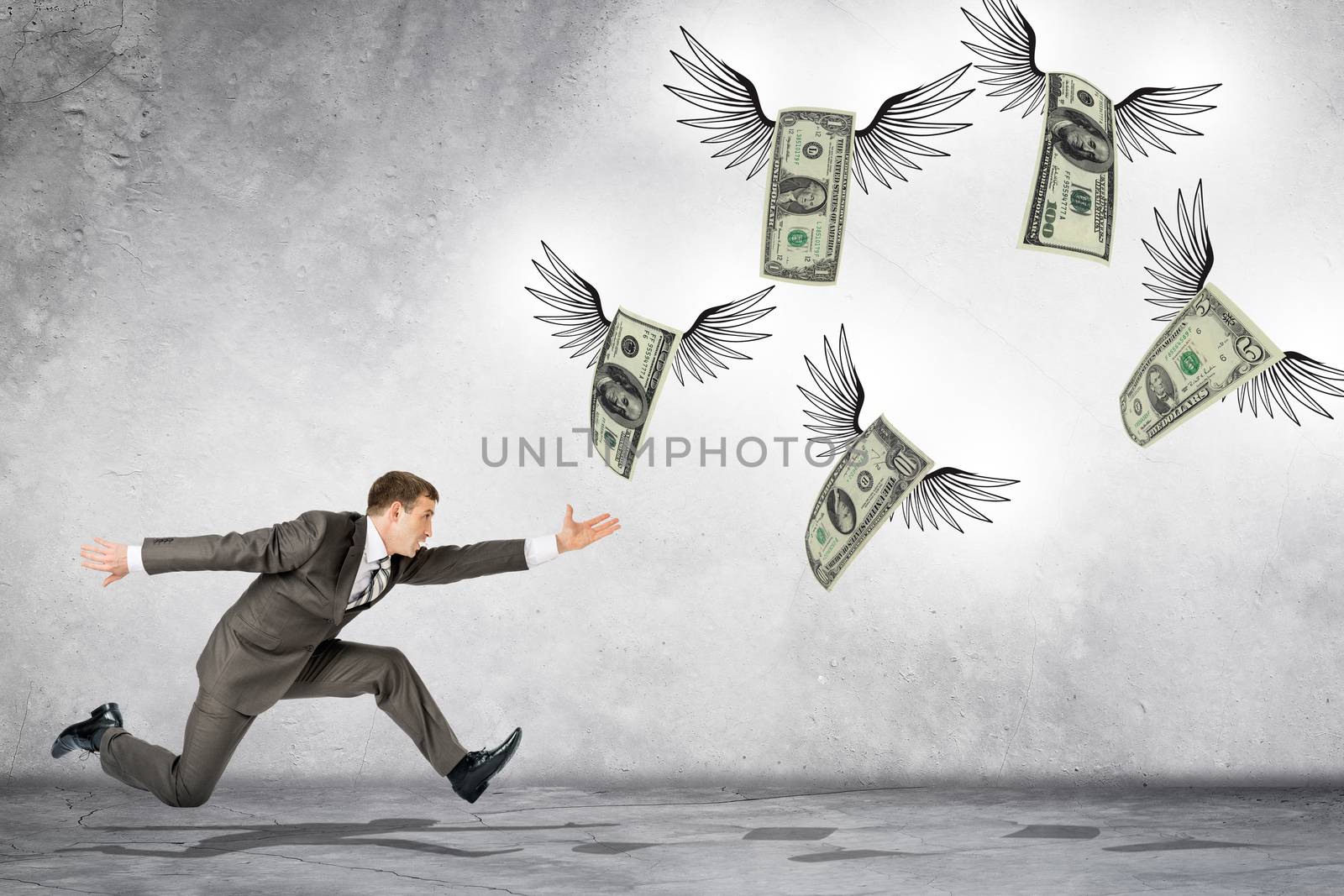 Business man running to catch flying dollars on gray background