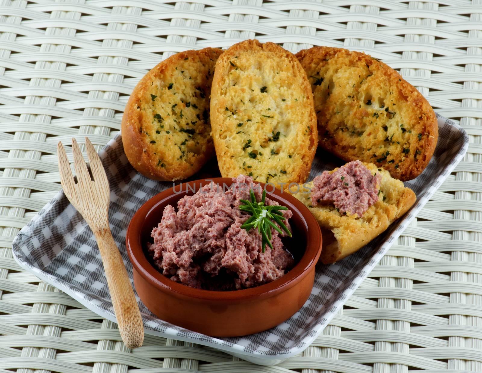 Delicious Homemade Meat Pate with Crispy Herbs Bread in Checkered Tray closeup on Wicker background