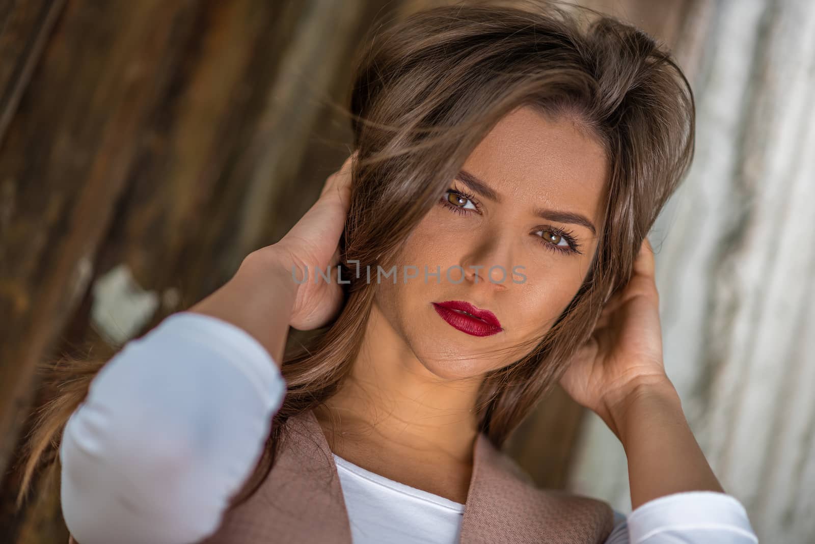 Young woman with red lips and brown hair is posing against the rustic wall. Shallow depth of field, dutch angle.