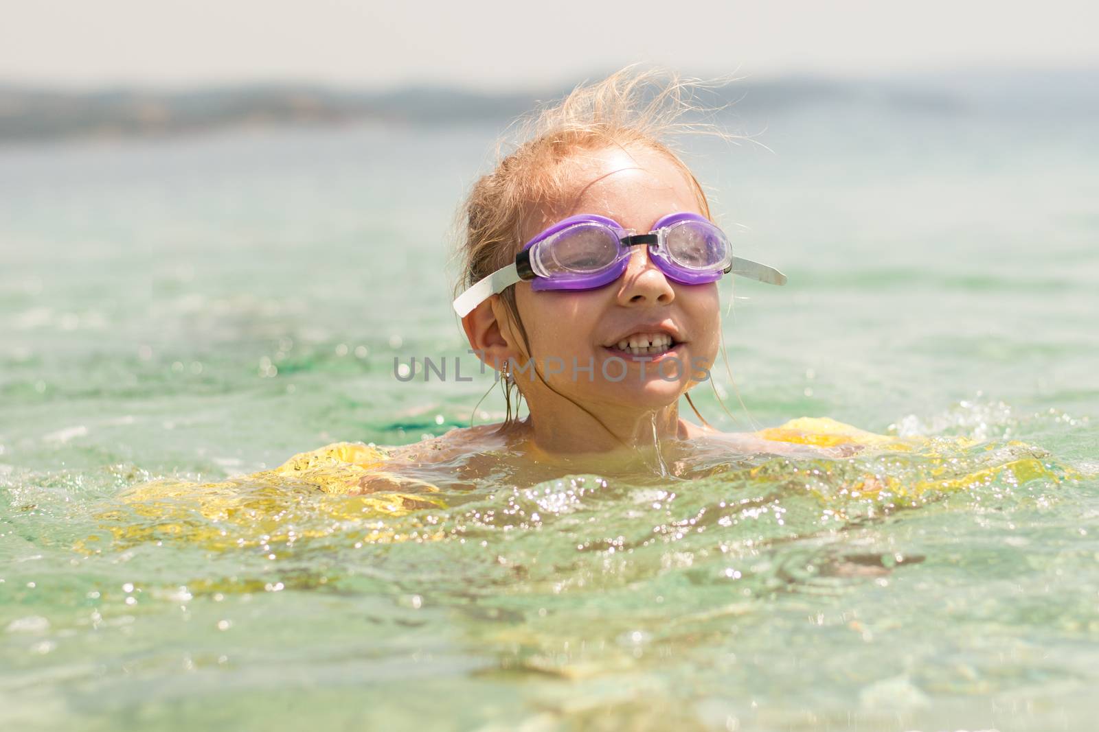 Cute little girl swimming with armbands and goggles in the sea