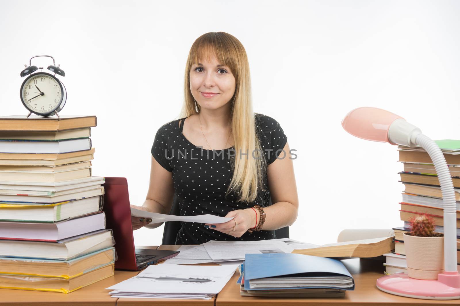 The girl behind the desk littered with books with a smile, holding a paper