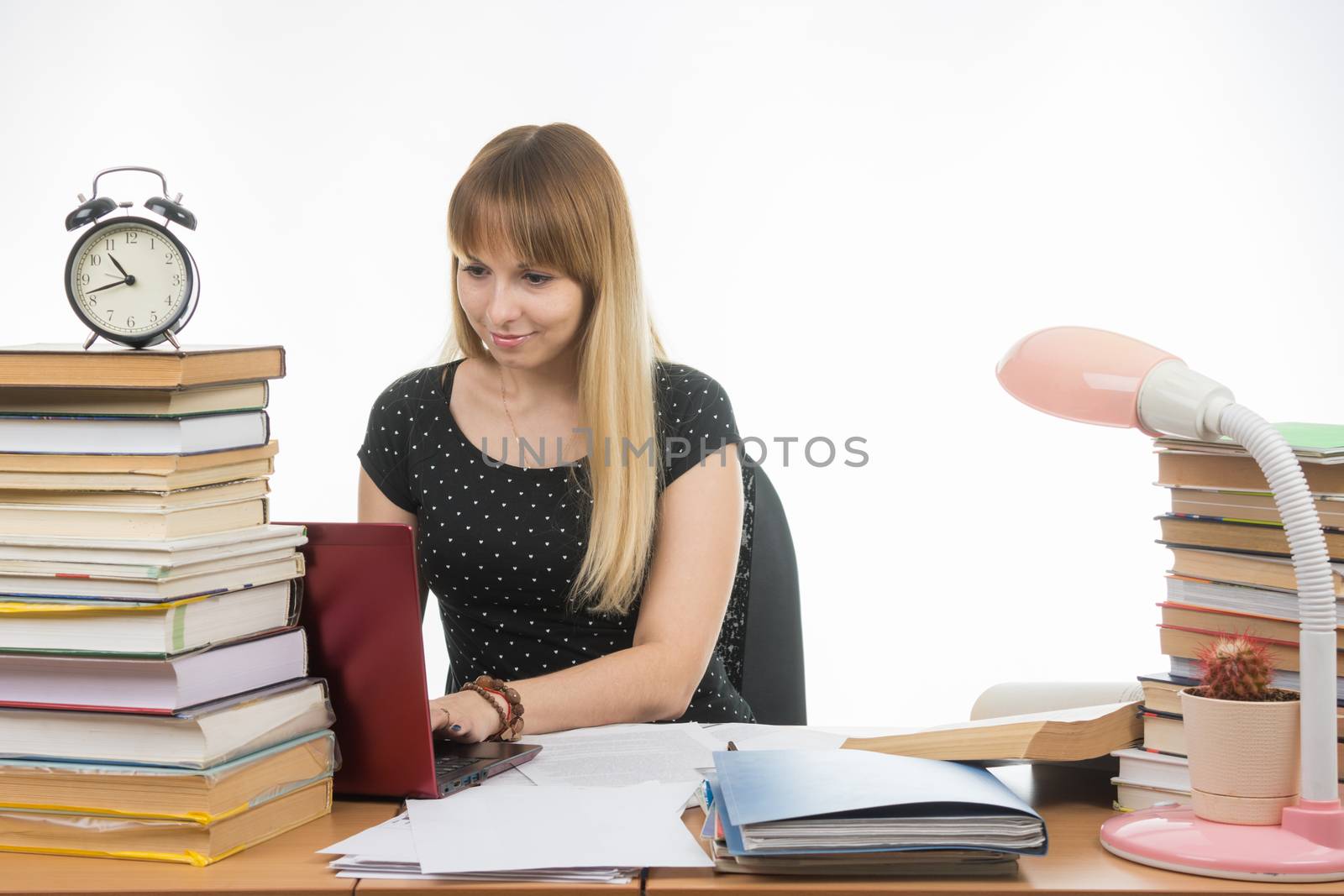 The girl behind the desk littered with books smiling in a laptop information gathering