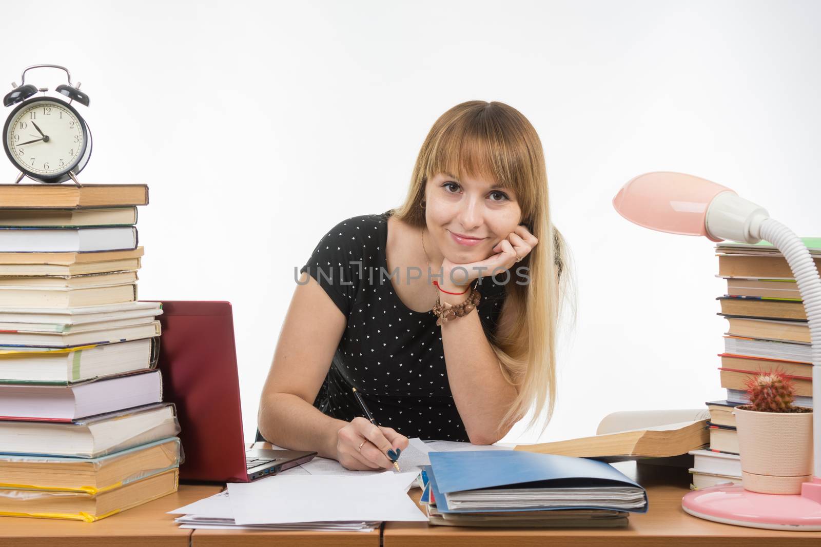  She is engaged at the table cluttered with books in the library with a smile looks in the frame