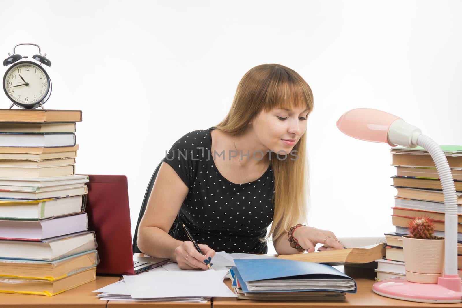 Pretty female student at a table littered with books in the library writing job