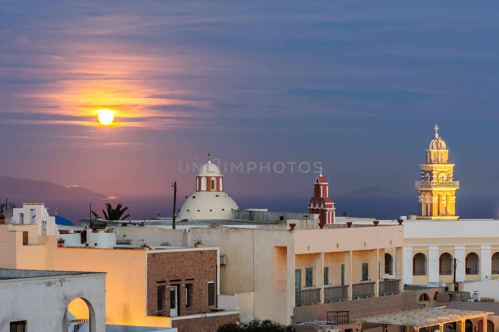 Illuminated buildings, domes and towers of of Fira at night, Santorini, Greece. Moon at sky.