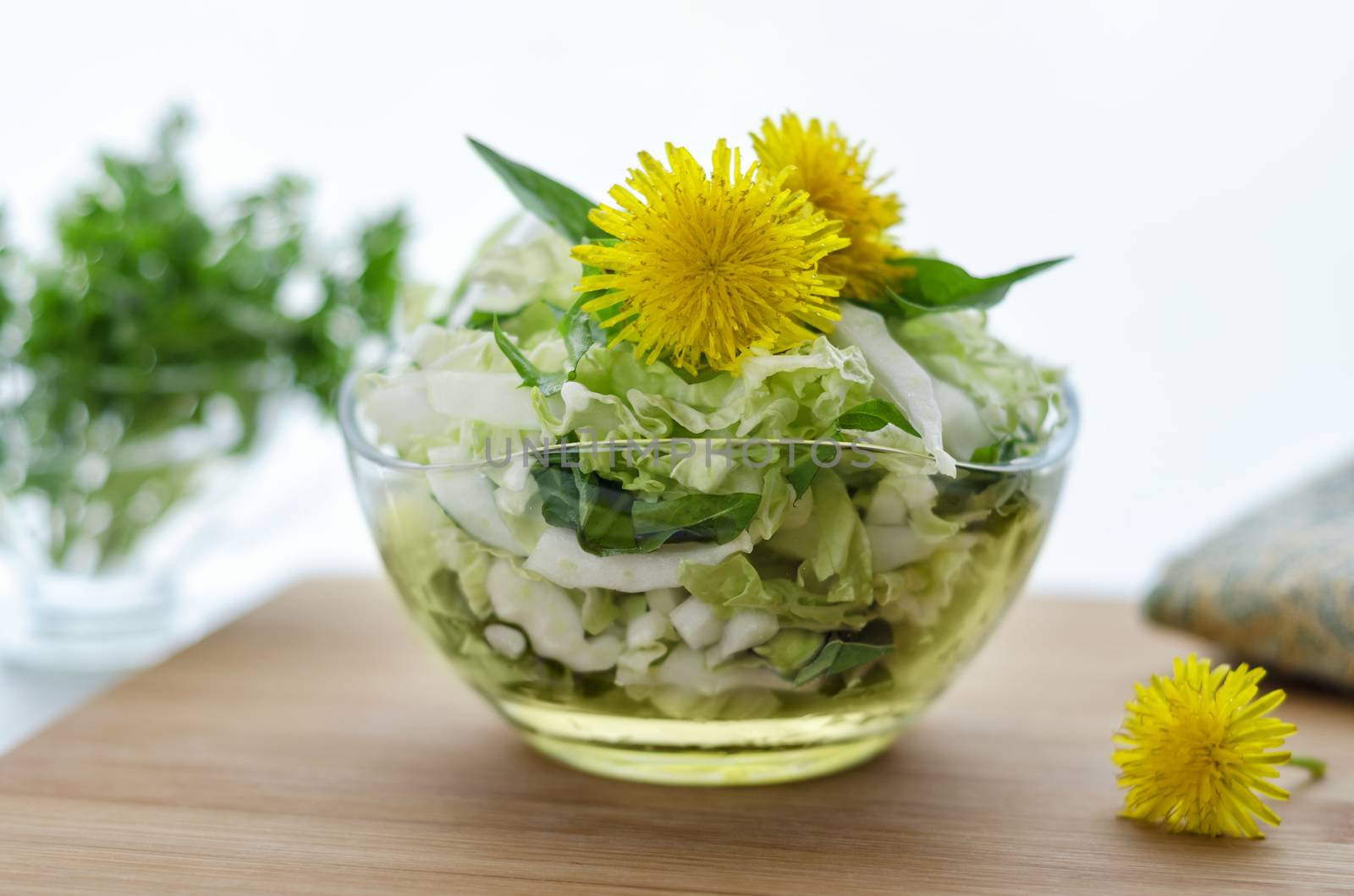 Salad from Chinese cabbage and dandelion leaves, on the table. Morning light, bokeh, decorated with flowers of the dandelion greens in the background and a napkin.