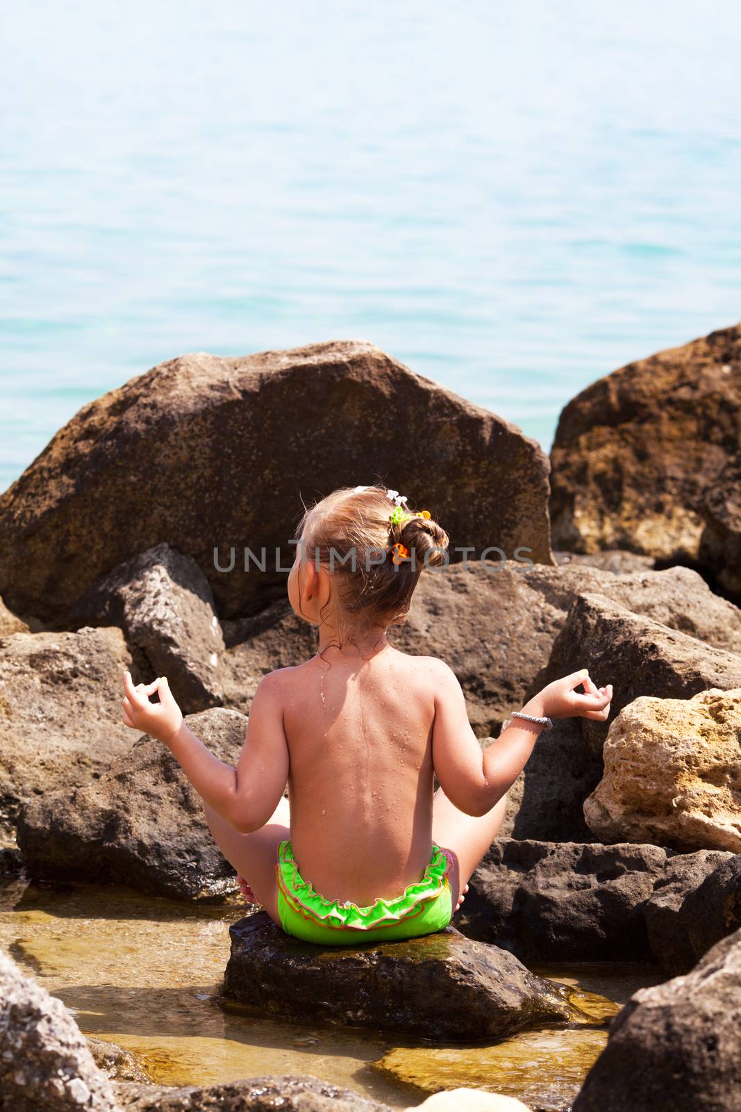 Little girl doing yoga on rocks by the sea