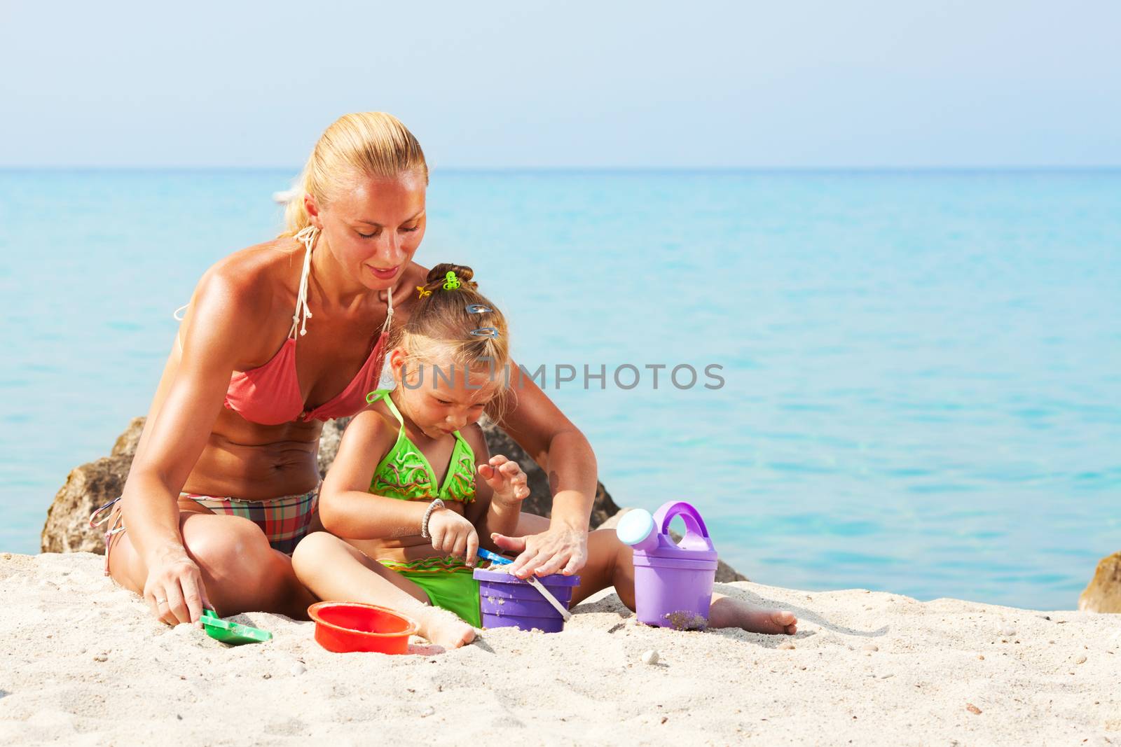 Mother and daughter playing on the beach with bucket and spade