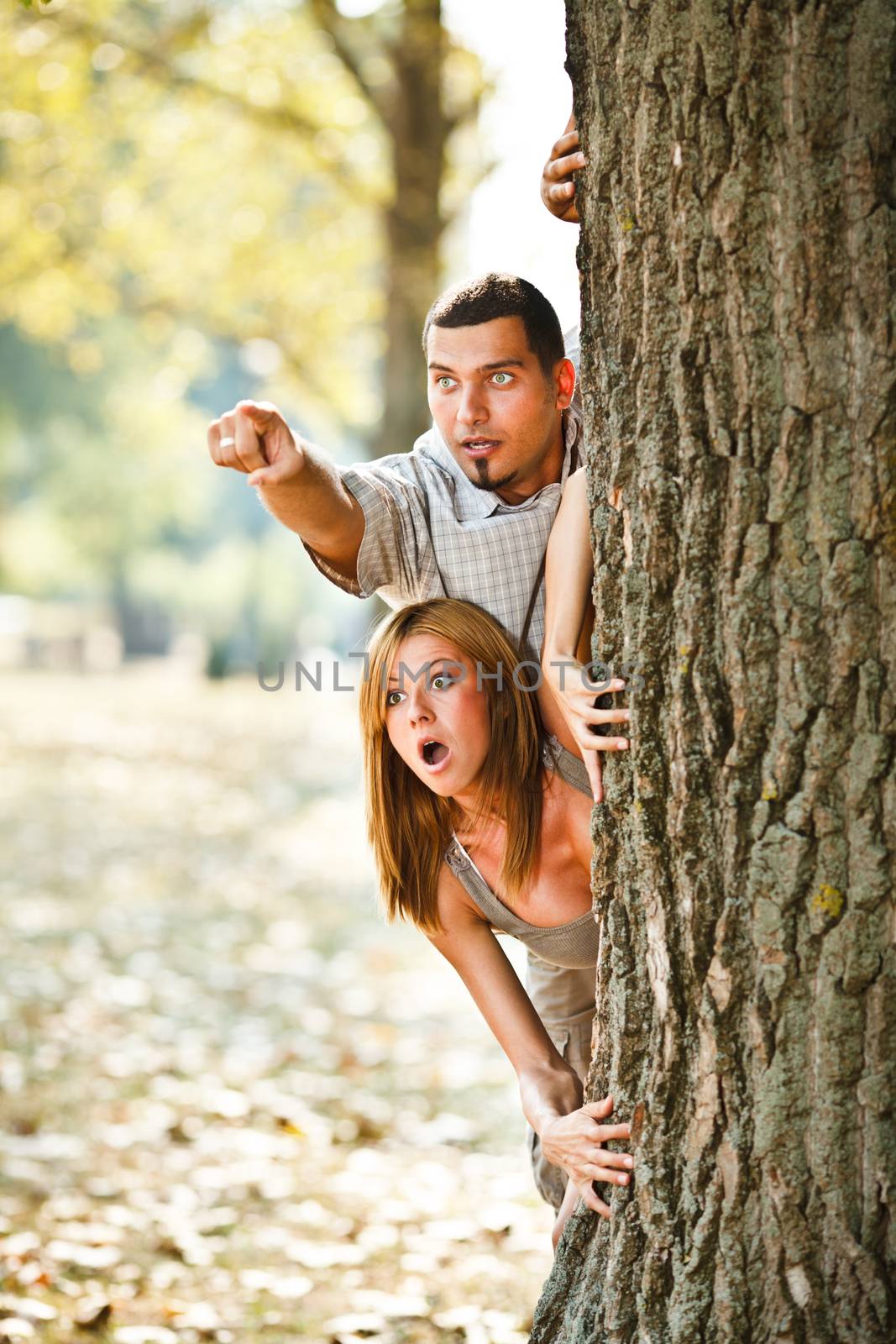 Young couple behind tree looking something scary