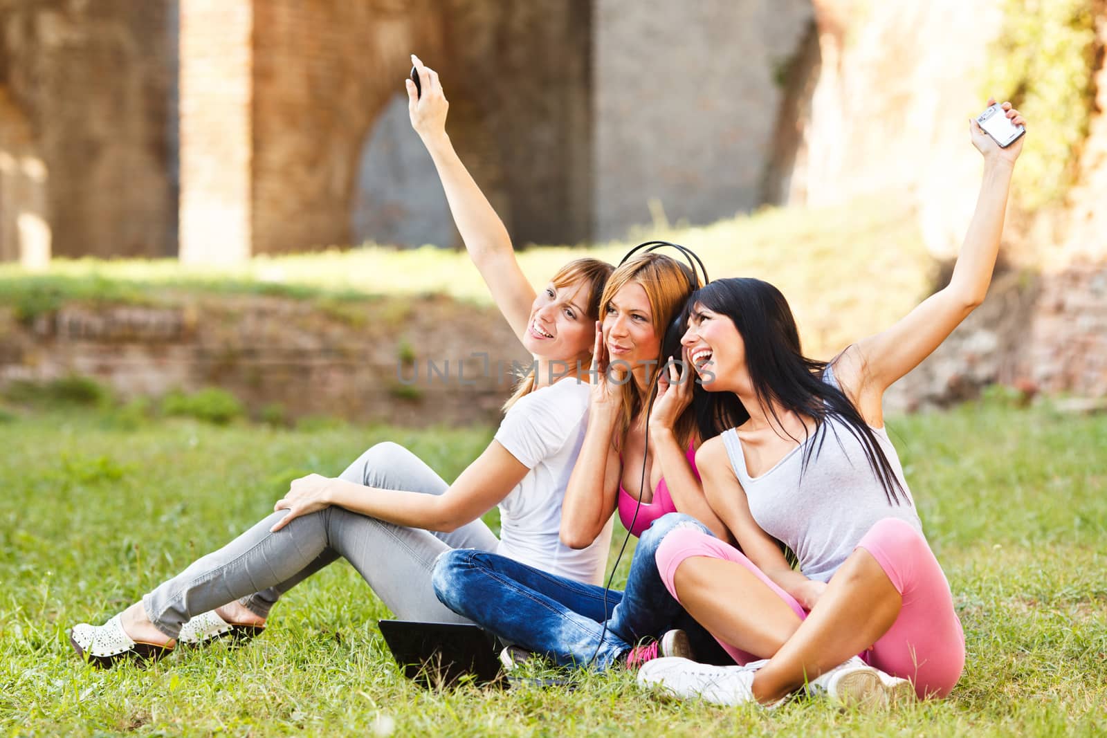 Three young beautiful girls listen music from notebook, outdoor