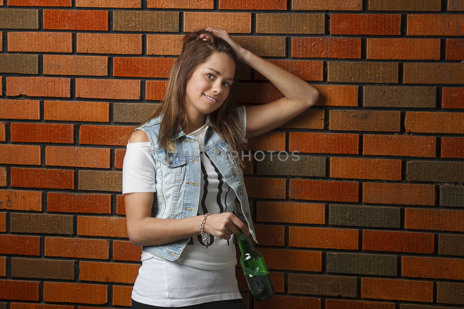 Young woman against a brick wall, holding a beer