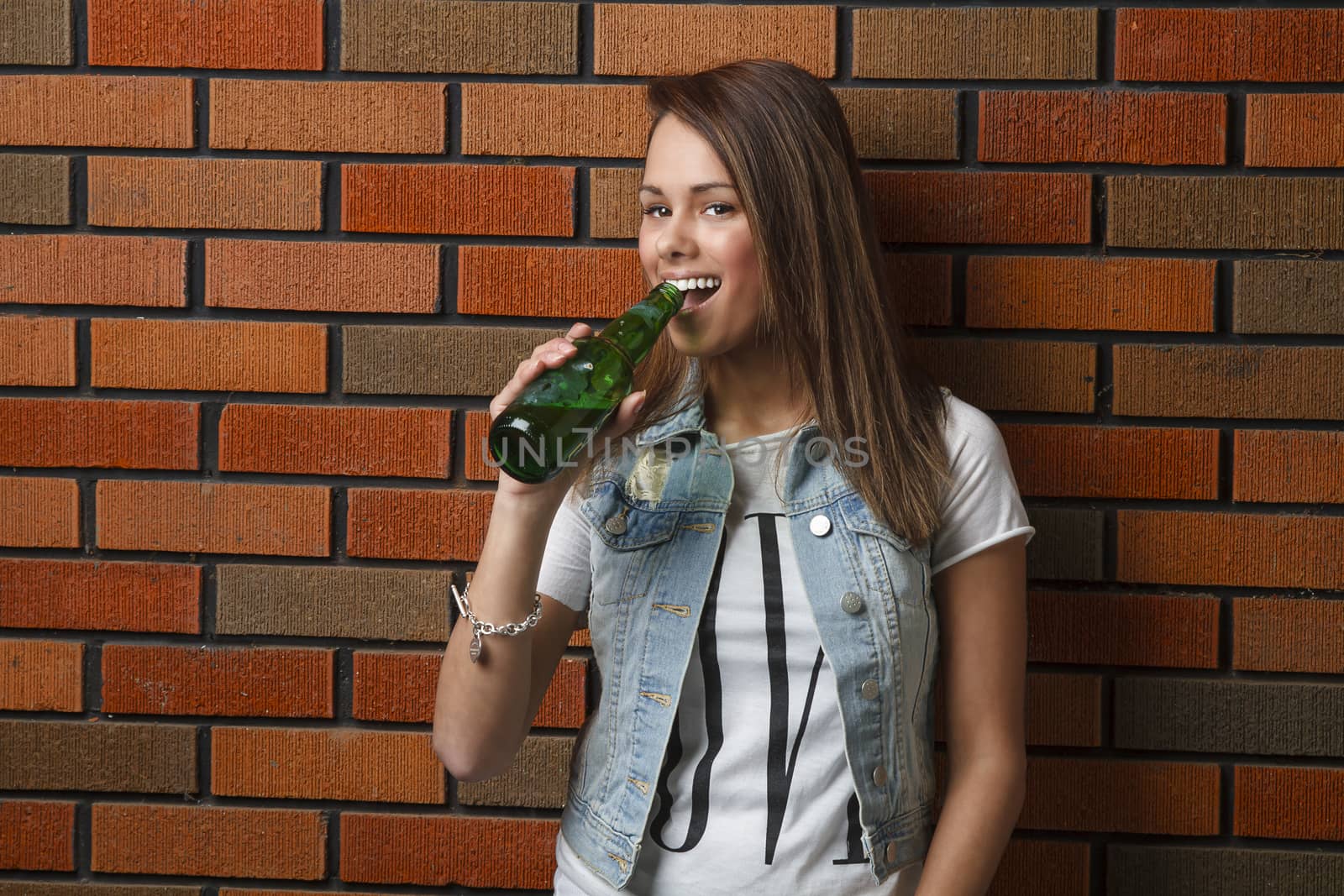 twenty something girl leaning against wall drinking a beer