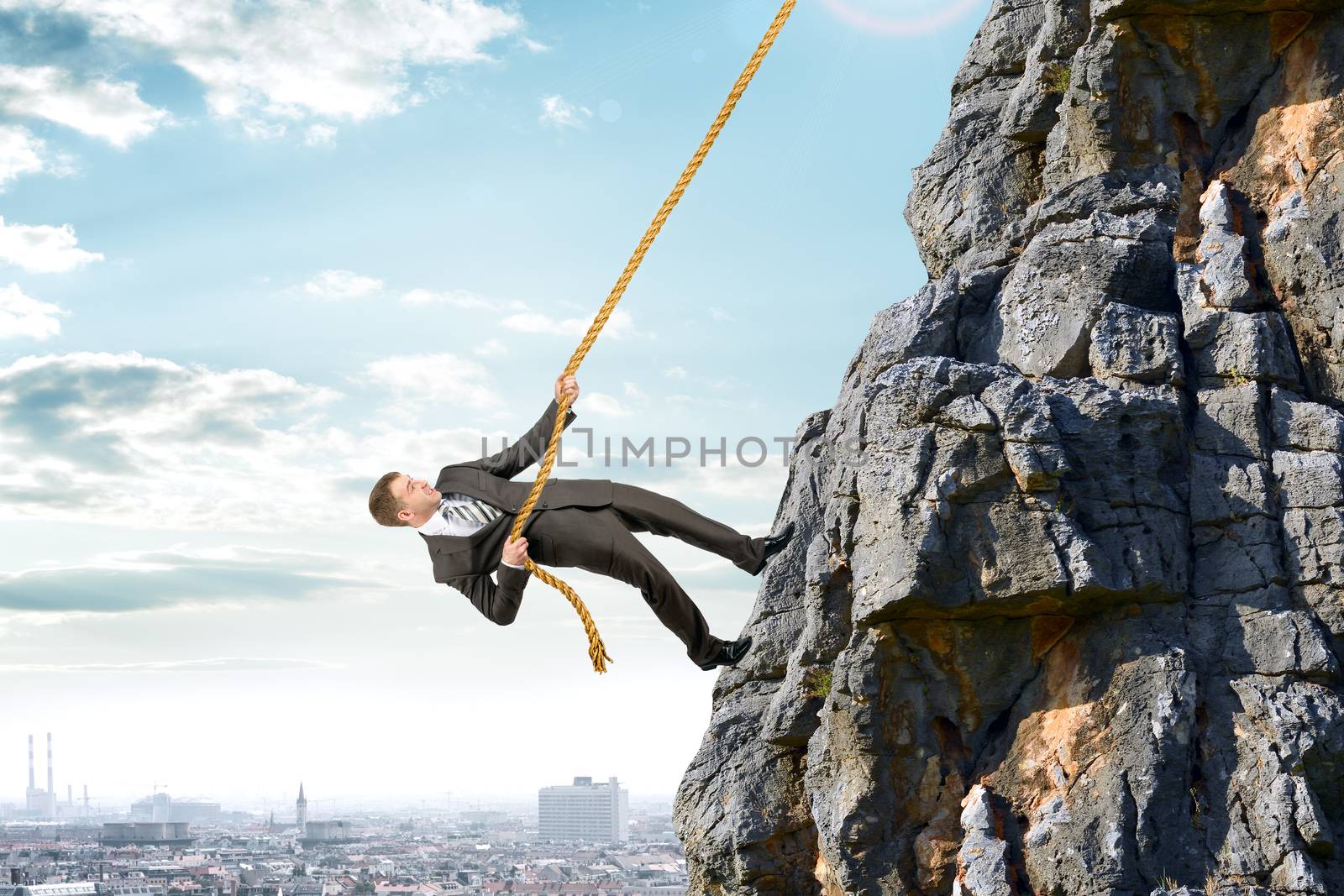 Business man in suit climbs mountain with rope