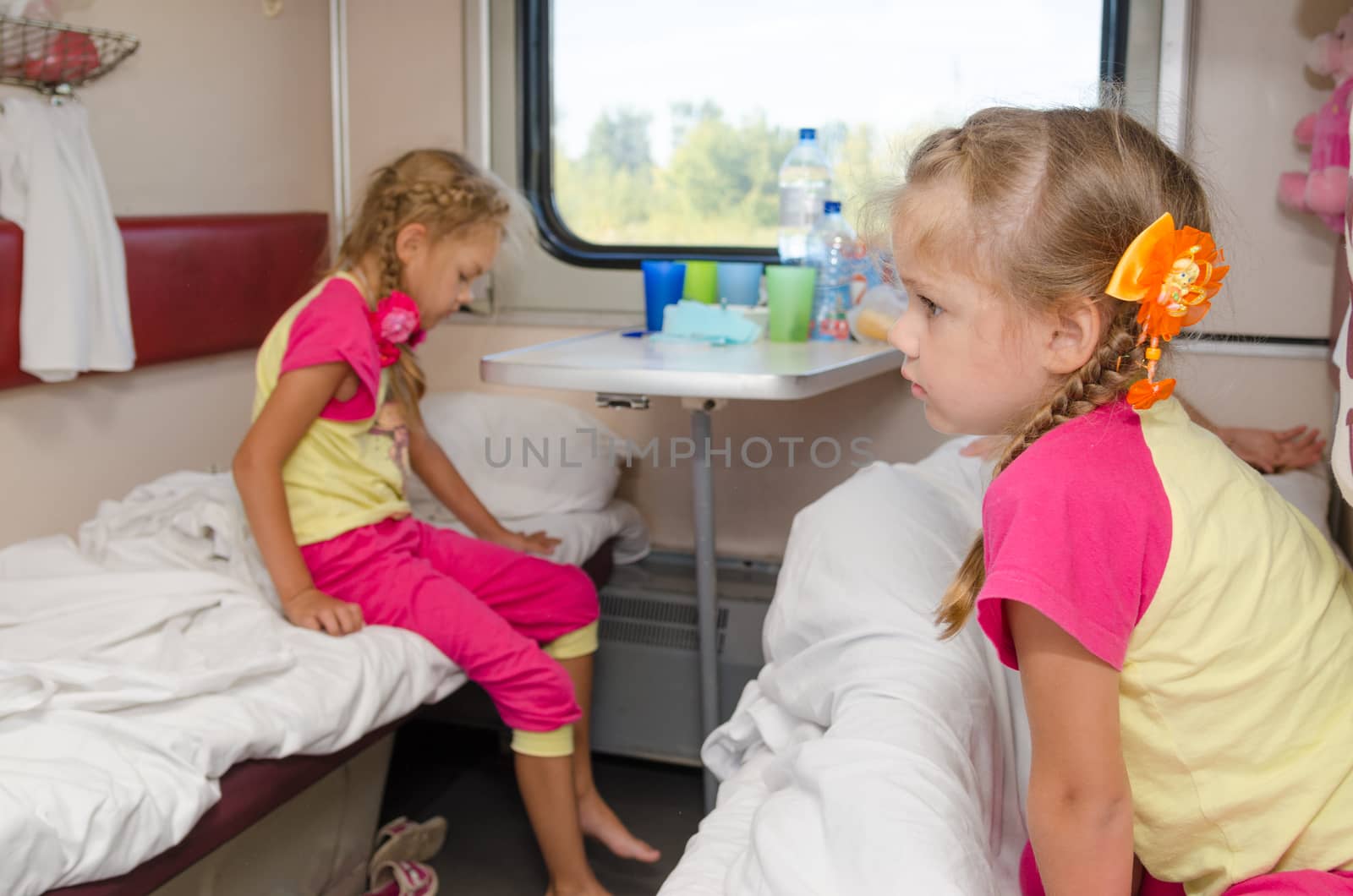 Two girls sisters on the train on the lower ground in the second-class compartment wagon