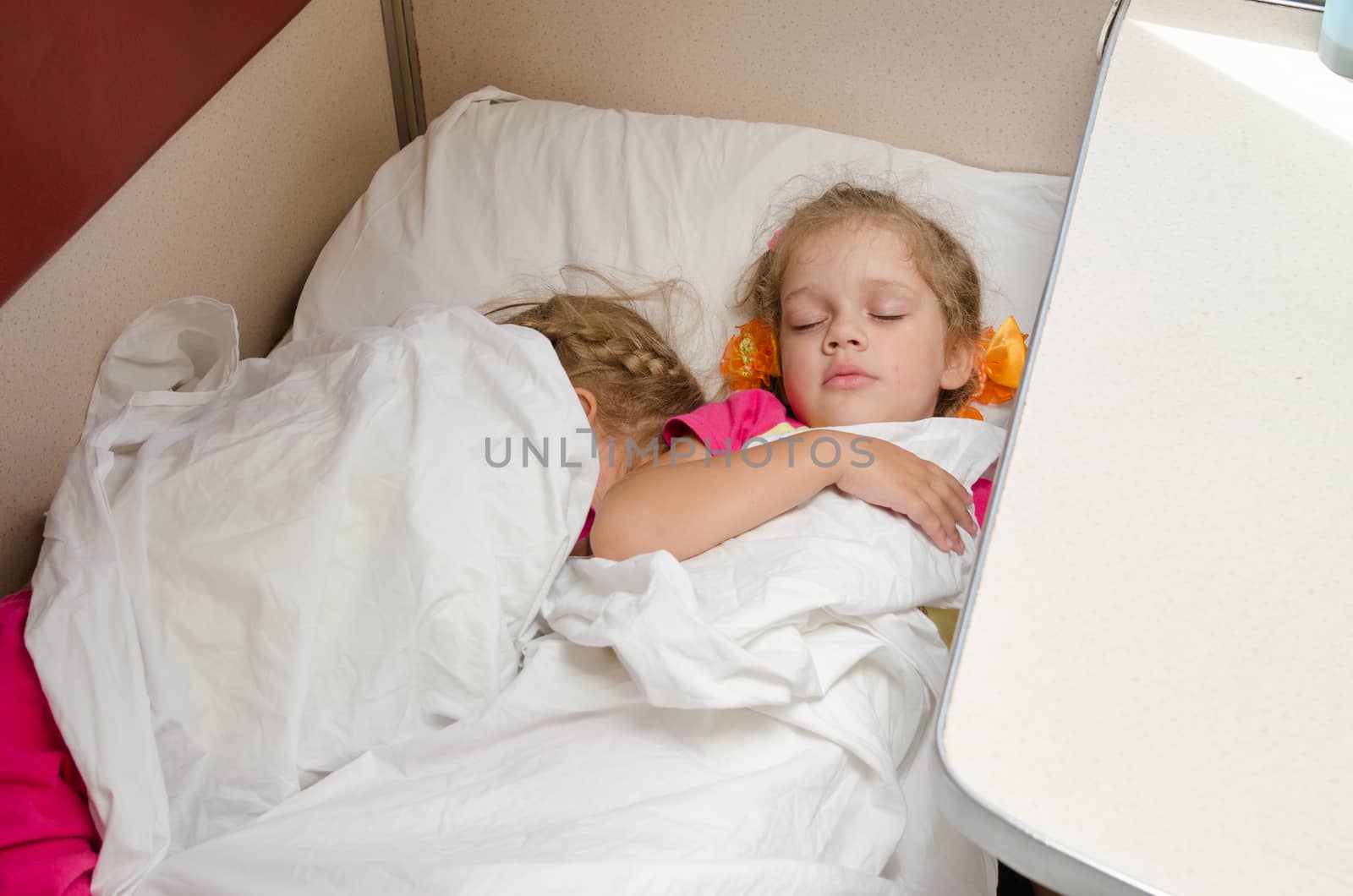 Two children sleep on the train on the same ground location in the second-class compartment wagon