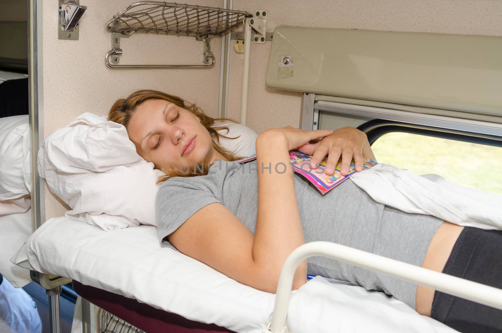 The girl in a train sleeping at the back on the top shelf and the side with the magazine in an embrace