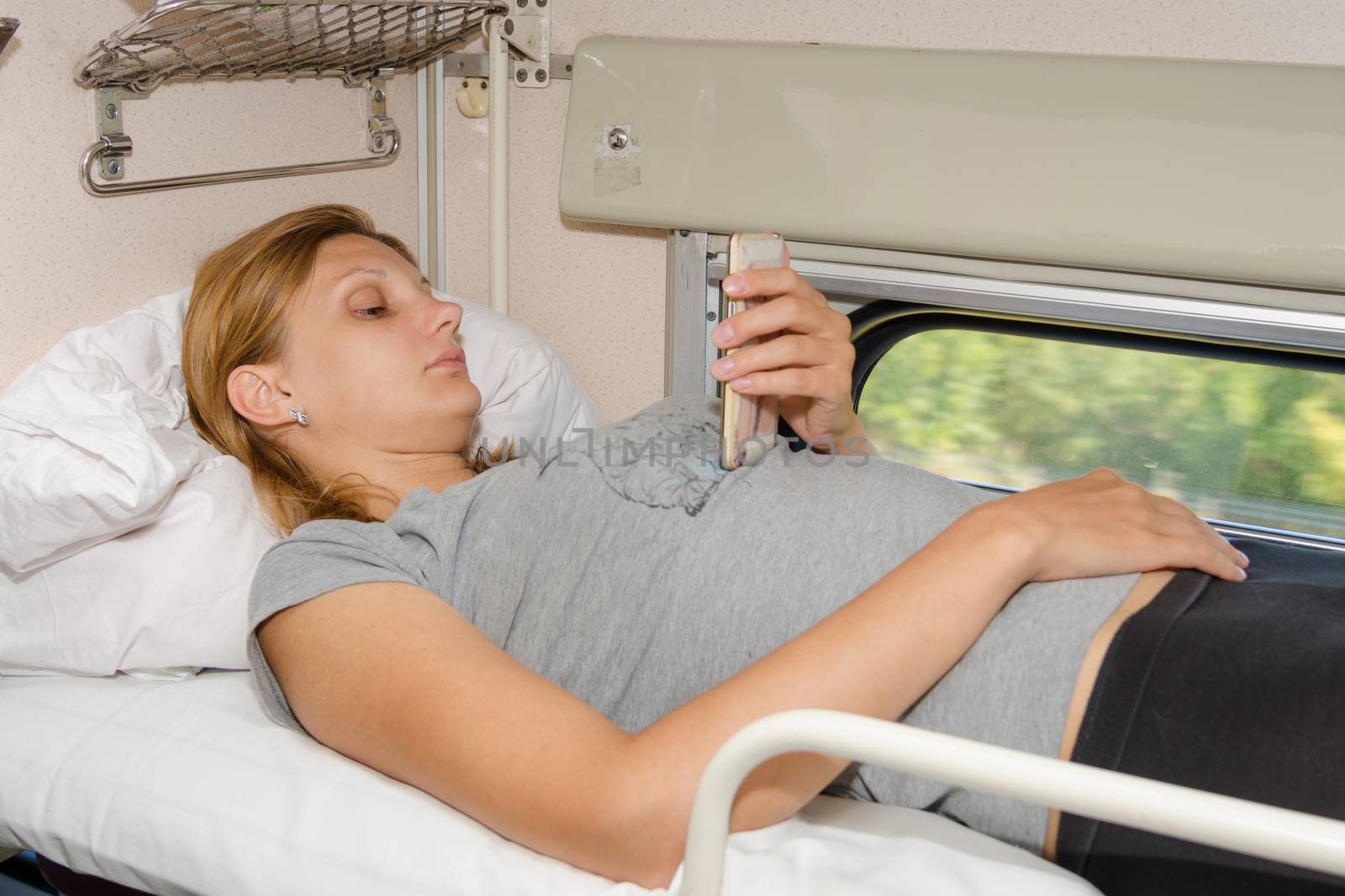 Passenger train is on the top shelf of the side seats in the second-class carriage and looking at the phone