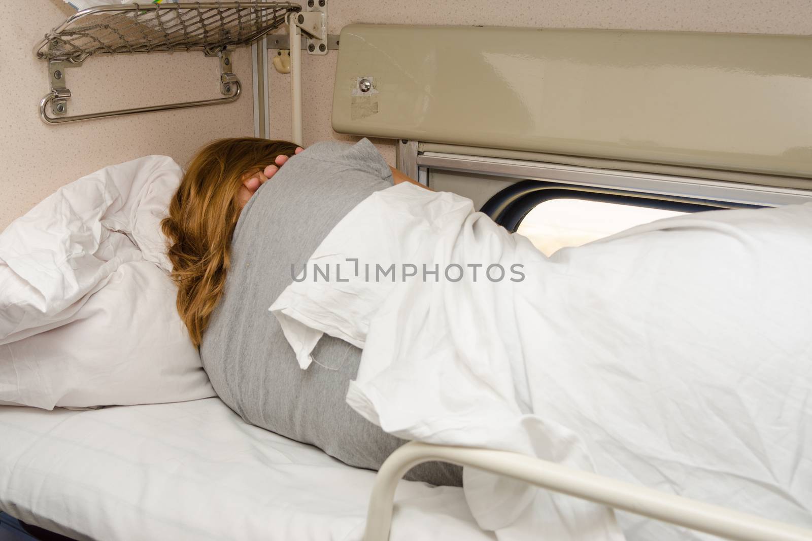The girl sleeps on the top shelf of the side seats in the second-class carriage turned to the wall