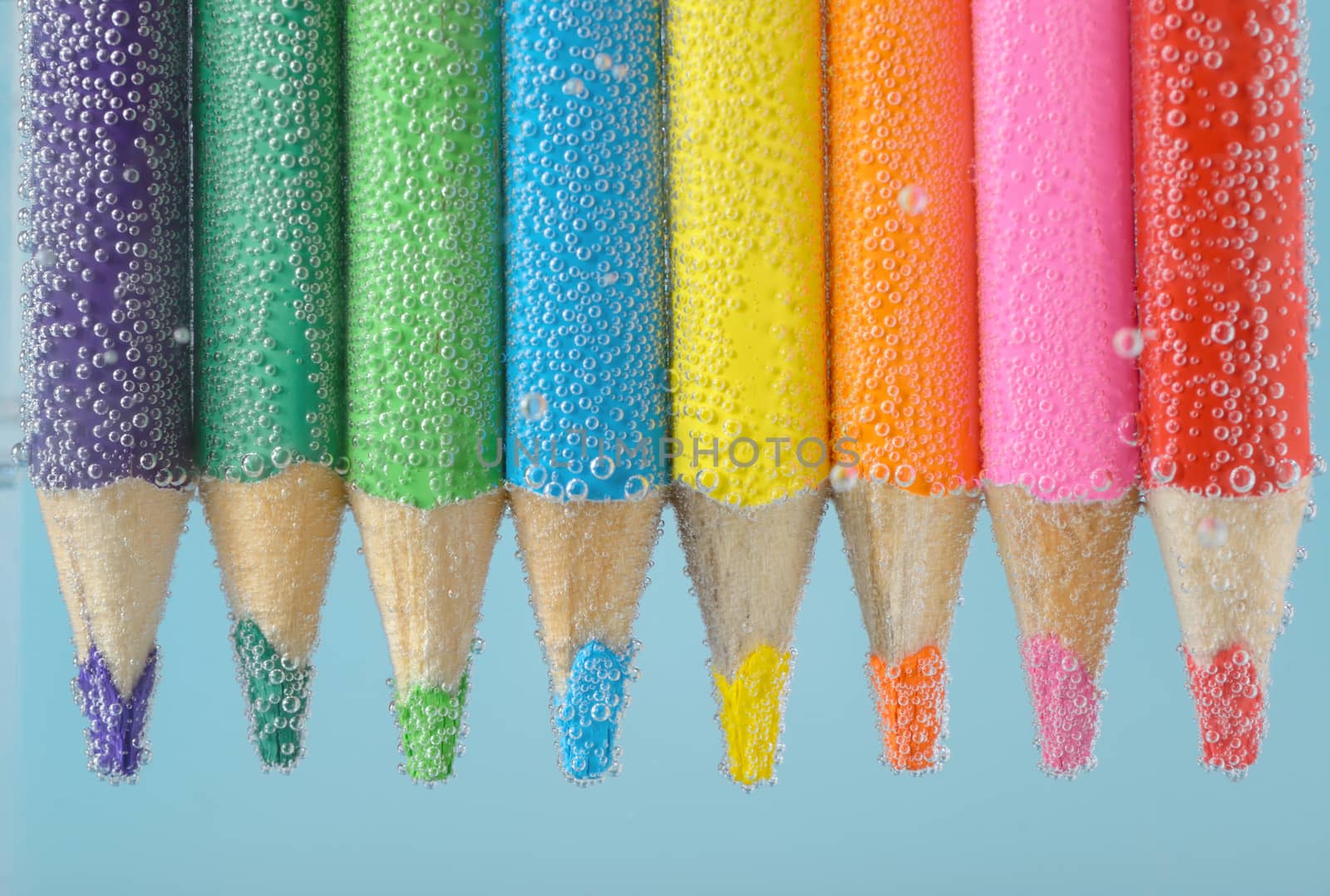 Colorful pencils close-up into water with bubbles