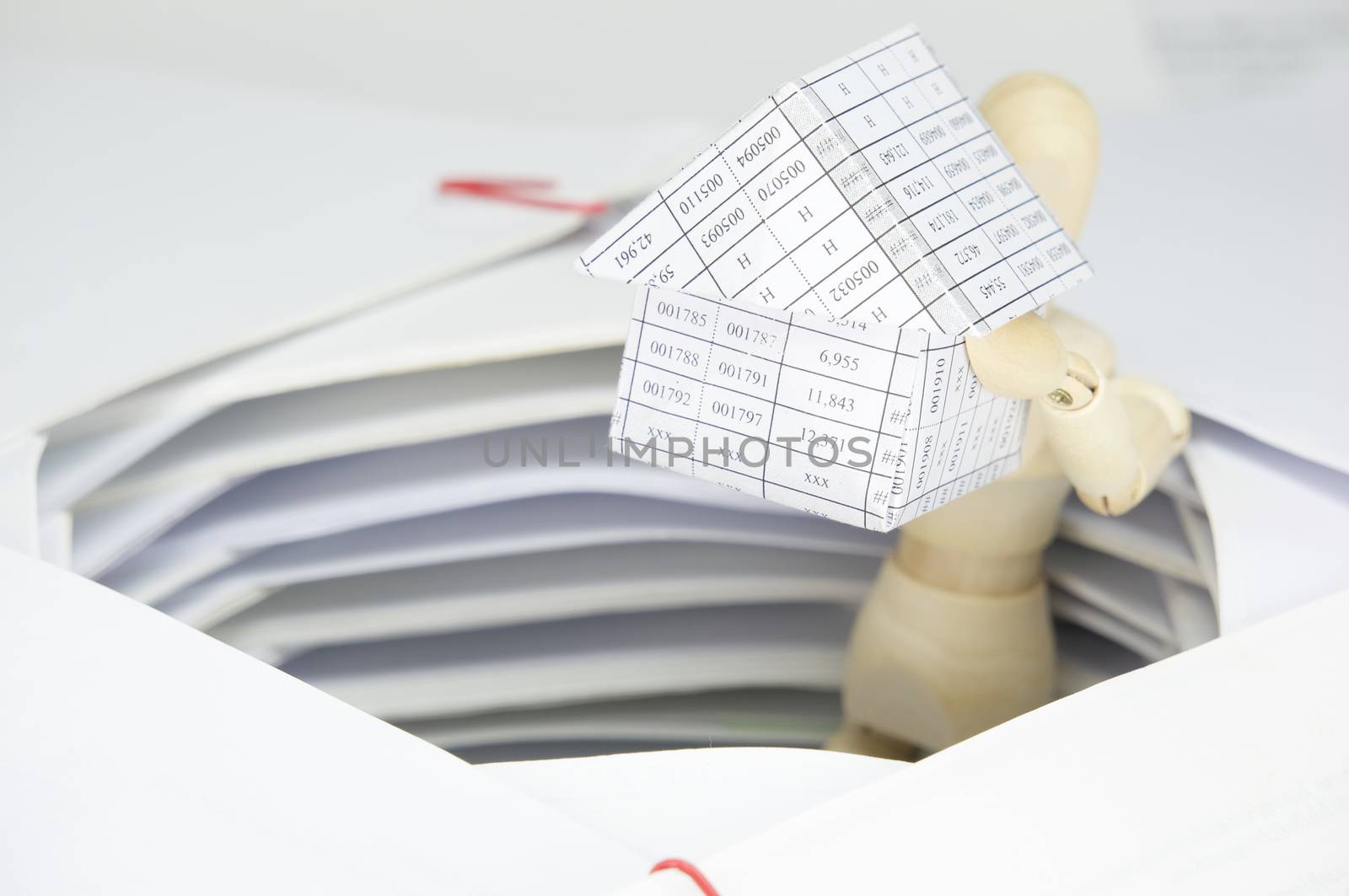 Wooden dummy holding house have surrounded by overload of paperwork by eaglesky