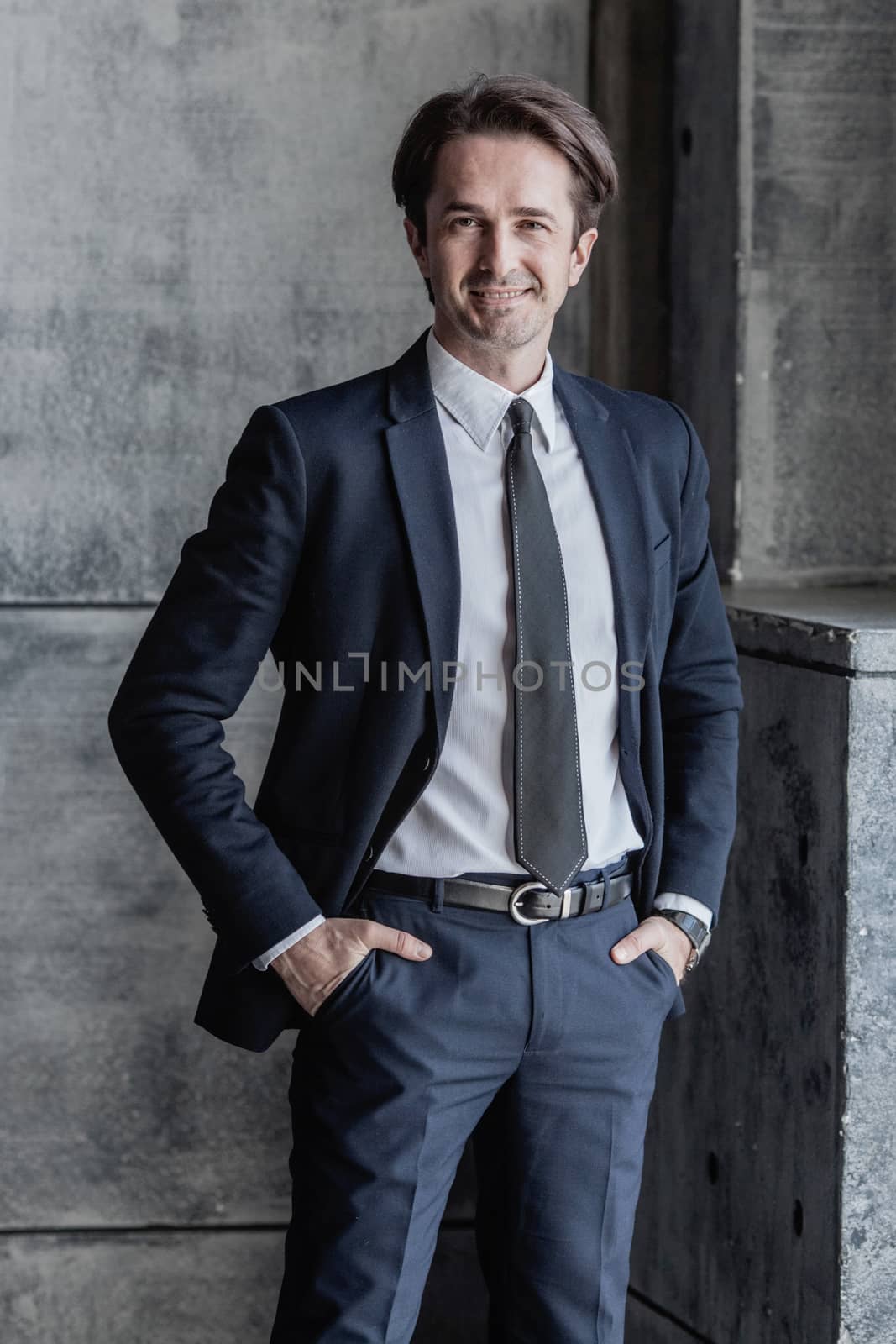 Portrait of smiling businessman in suit over concrete wall background