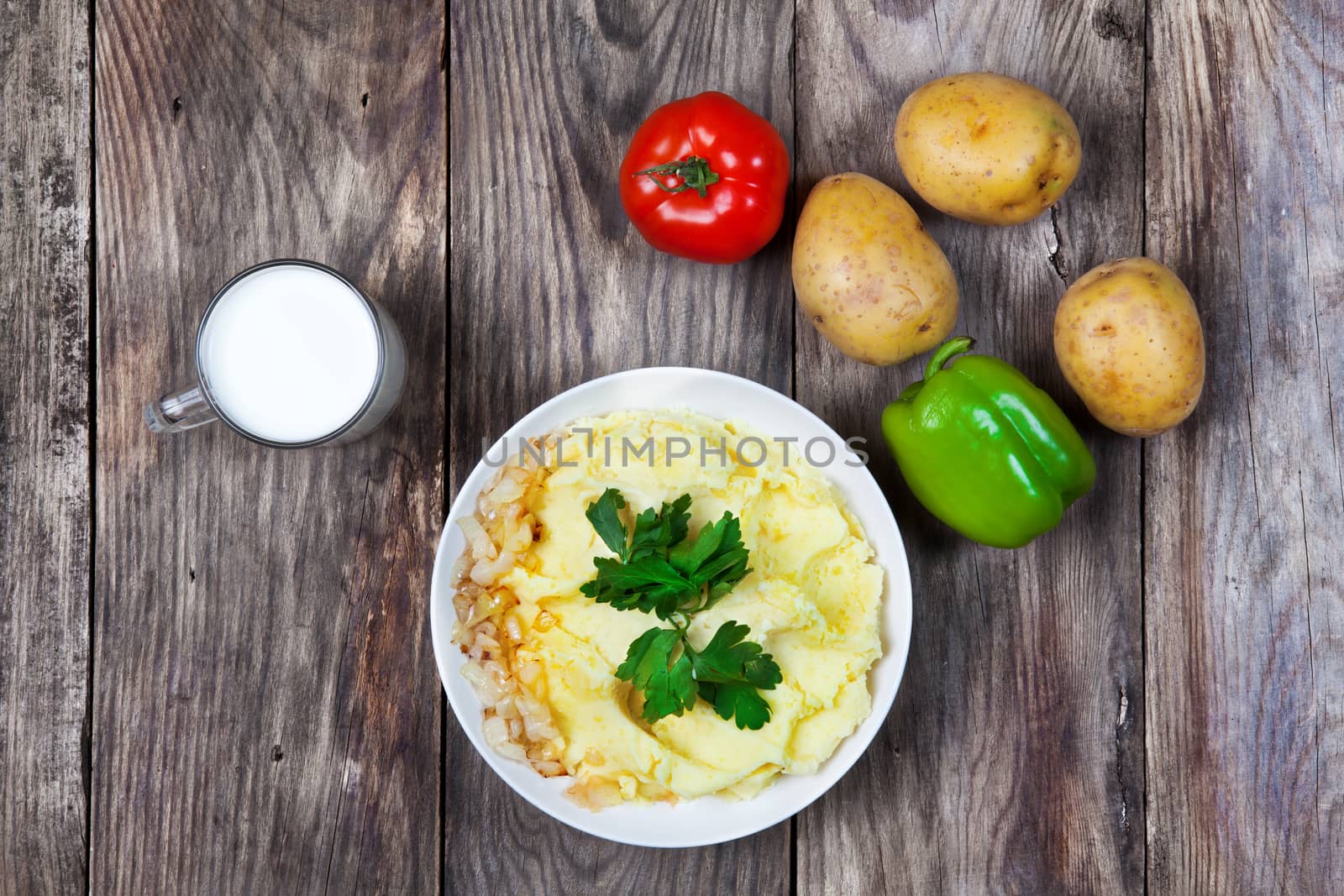 mashed boiled potato with herbs. milk and vegetables on a wooden background