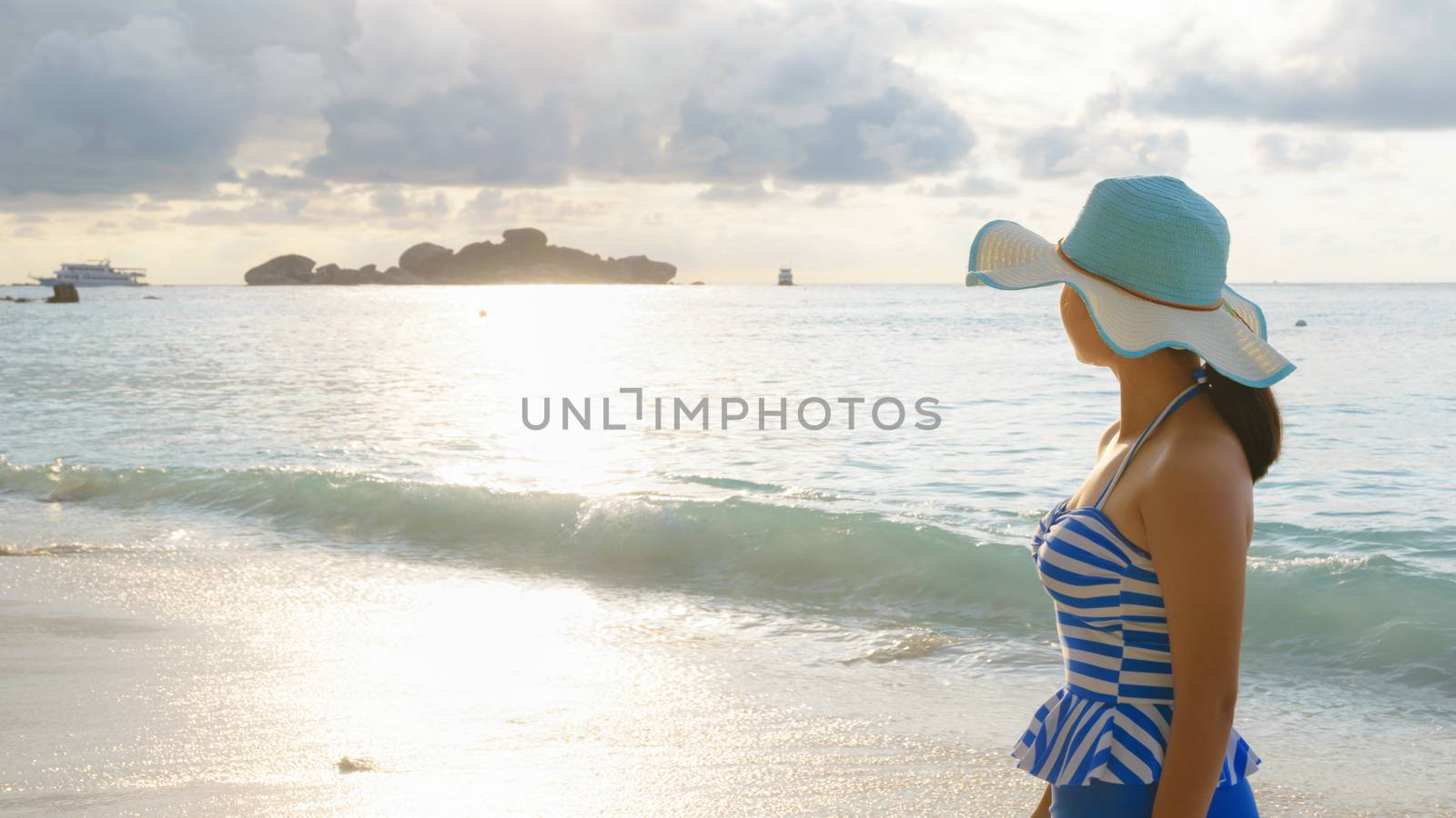 Young girl wearing a hat and swimsuit standing watch nature sky and sea during the sunrise on beach of Honeymoon Bay at Koh Miang, Similan Islands National Park, Phang Nga, Thailand, 19:6 wide screen
